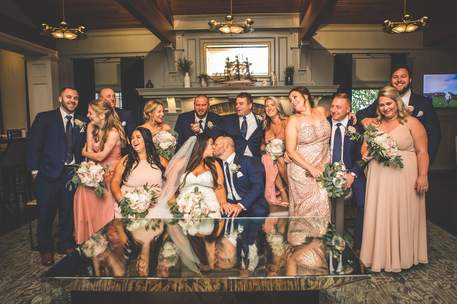 Wedding party poses together in an elegant indoor venue with warm lighting and rustic wooden beams.