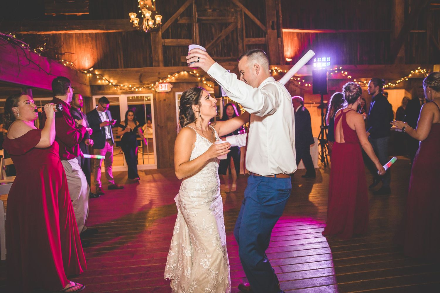 Wedding celebration with colorful purple lighting and guests dancing in a rustic venue.