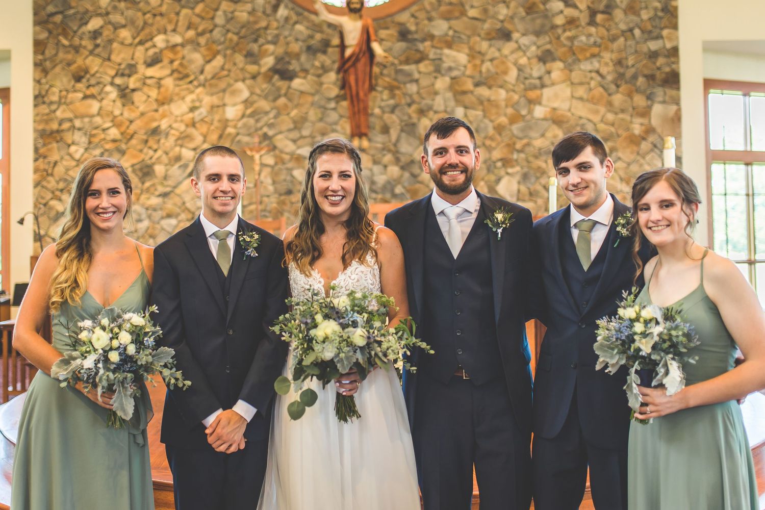 Large wedding party gathered for formal photos inside a stone church sanctuary.