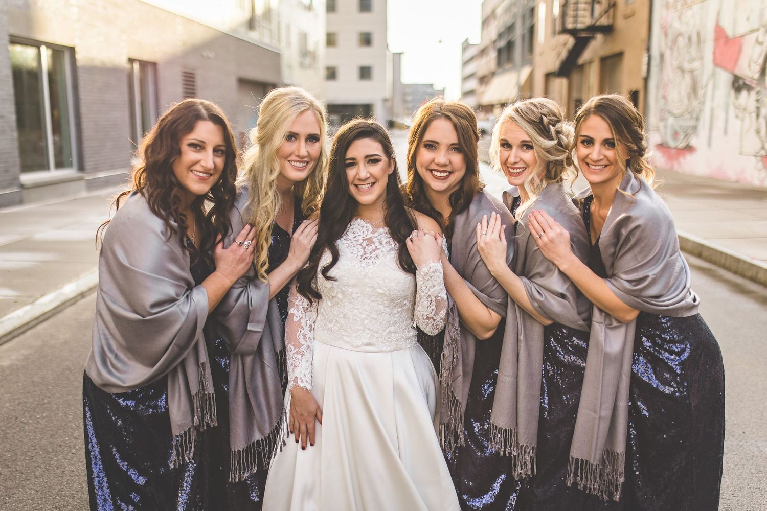 Wedding party bridesmaids in navy dresses pose together on urban street.