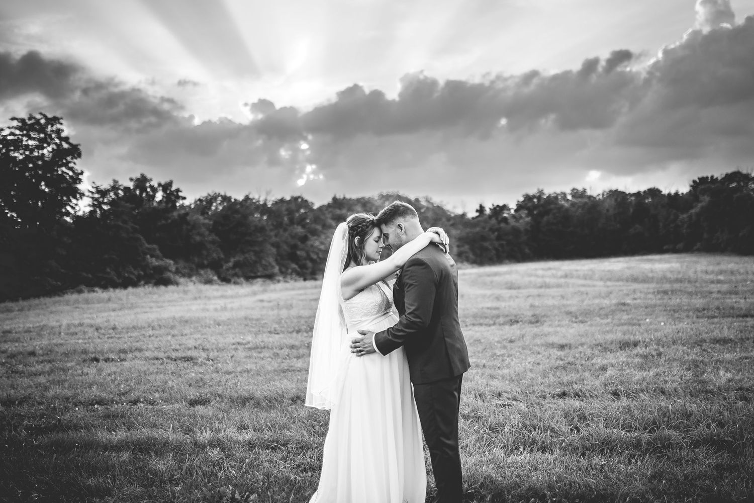 Black and white dramatic wedding portrait in an open field with cloudy sky.