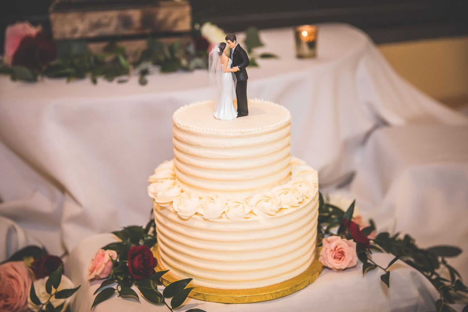 Elegant white wedding cake with textured frosting and floral decorations displayed at a reception.