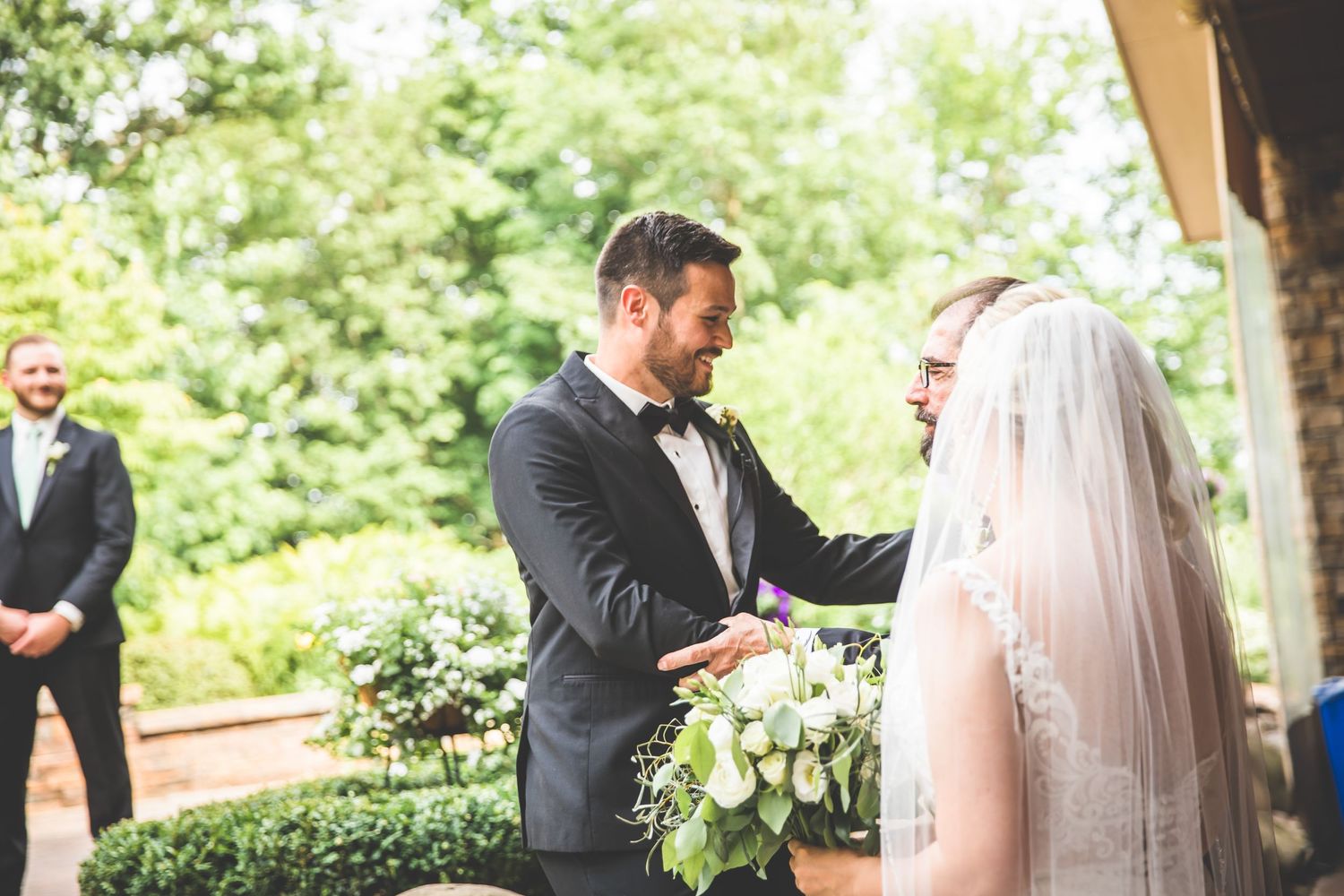 Intimate exchange between couple during outdoor wedding ceremony with natural backdrop.