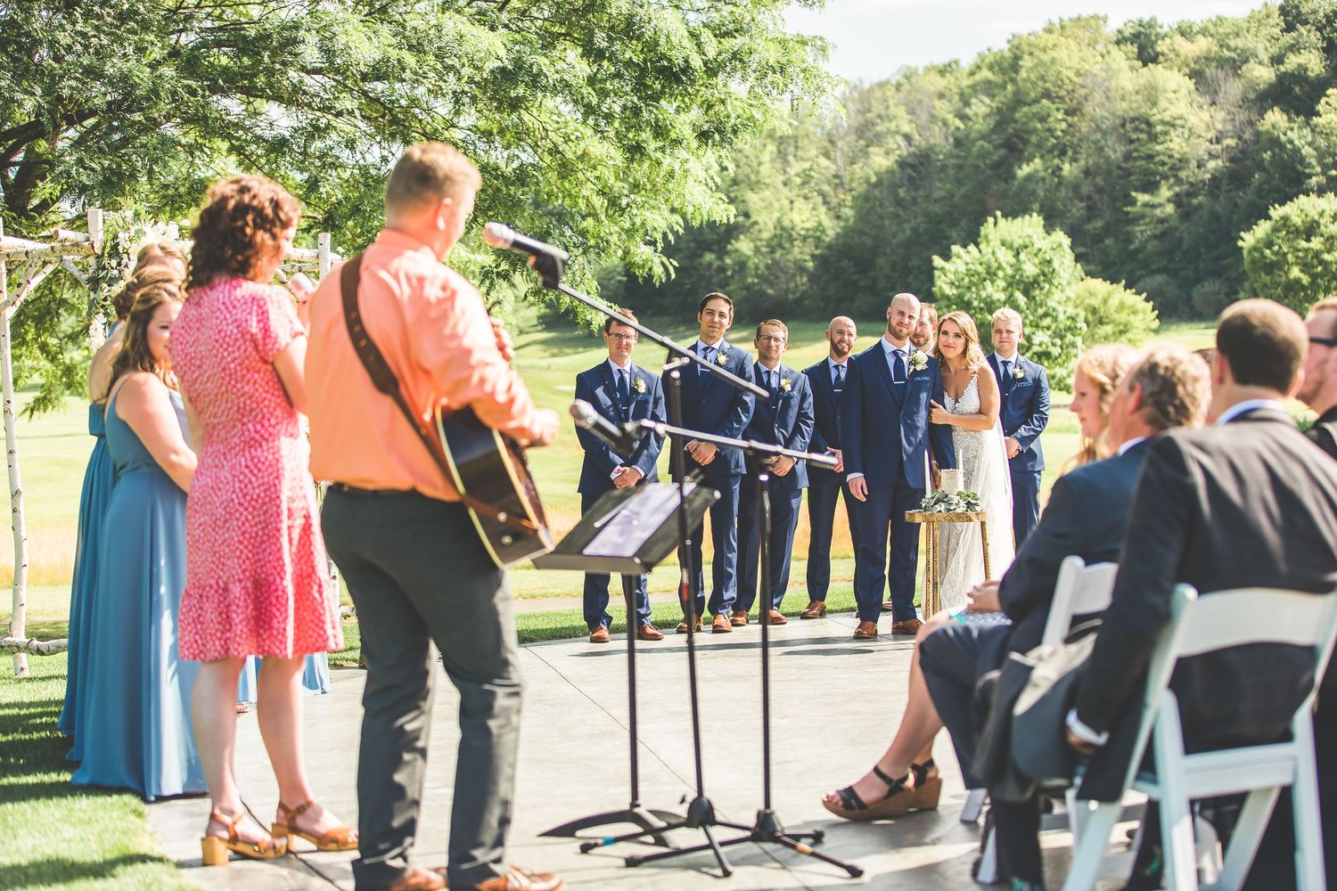 Outdoor wedding ceremony setup with white chairs and guests on a sunny day.