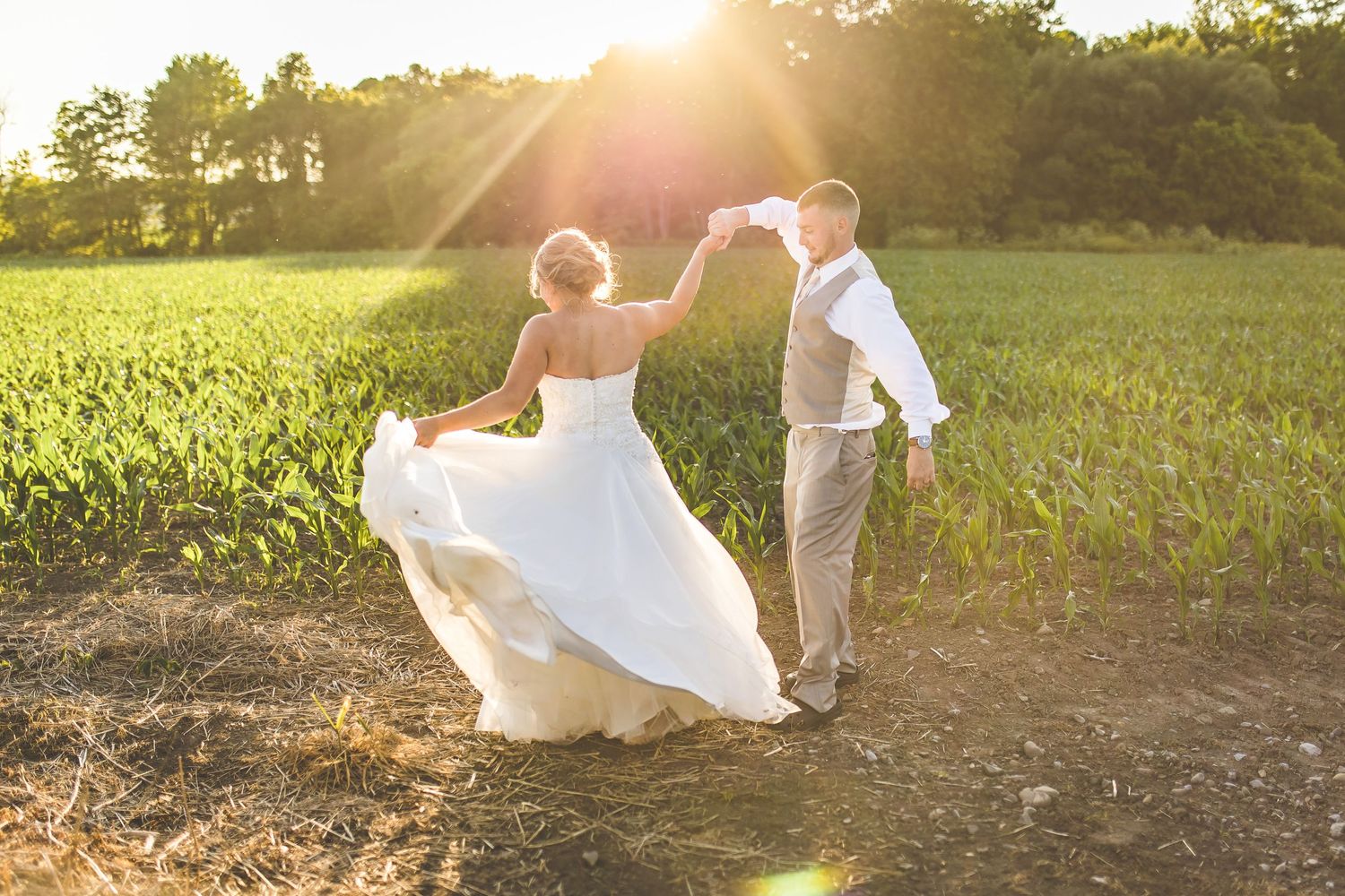 Newlyweds dancing together in a sunlit field at golden hour.