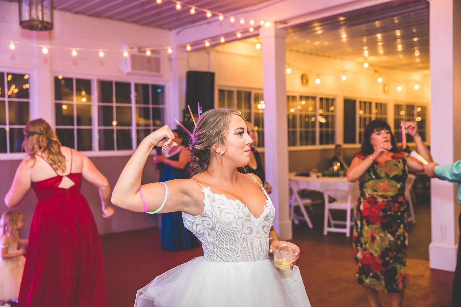 Wedding guests dancing and celebrating on a dance floor illuminated by pink and purple lighting.