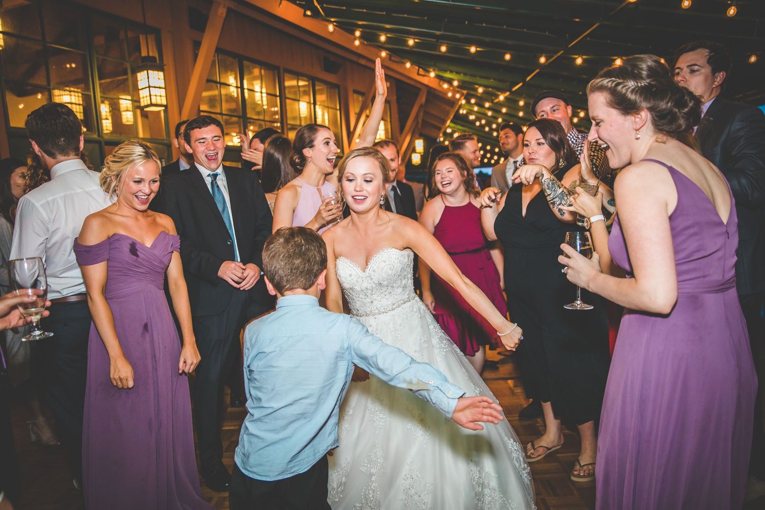 Wedding guests dancing and celebrating on a rustic dance floor under string lights.