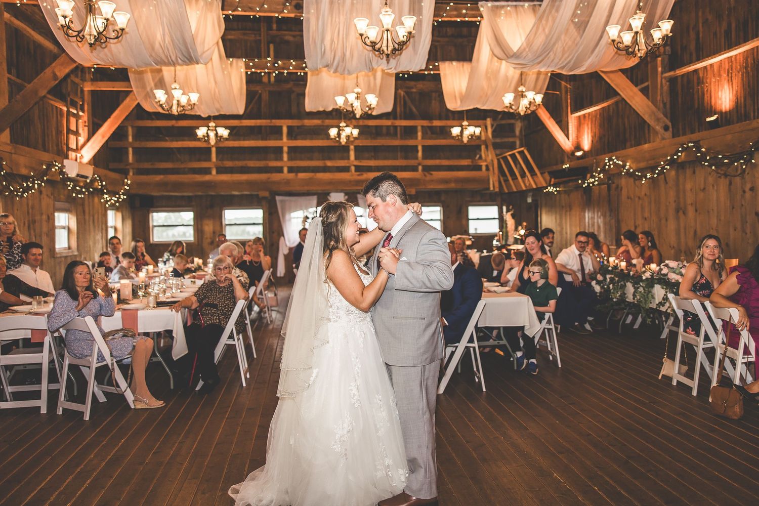 Wedding reception dance in rustic barn venue with exposed beams and romantic lighting.