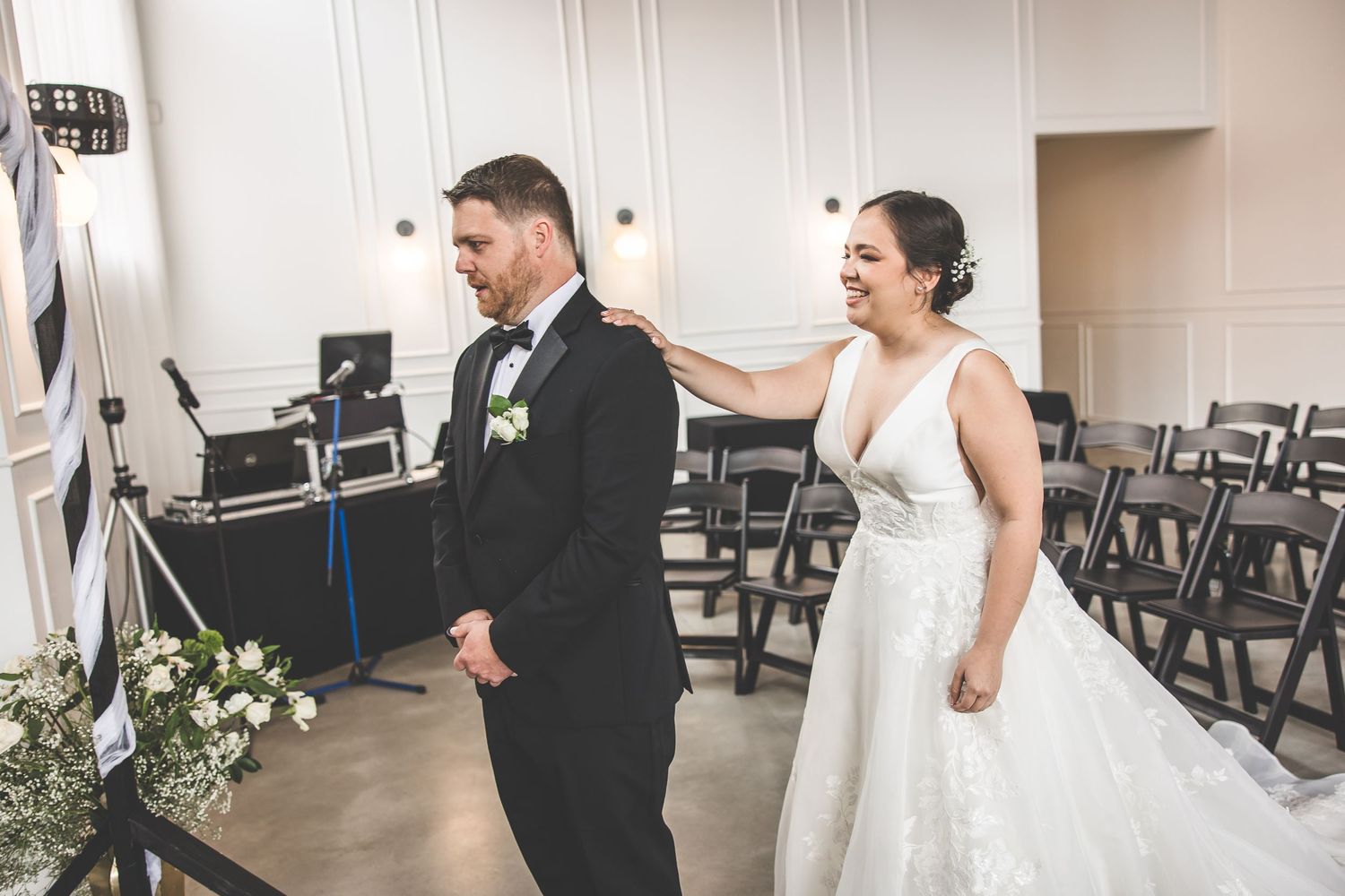 A couple shares a joyful moment during their first look in an elegant white room with black chairs.