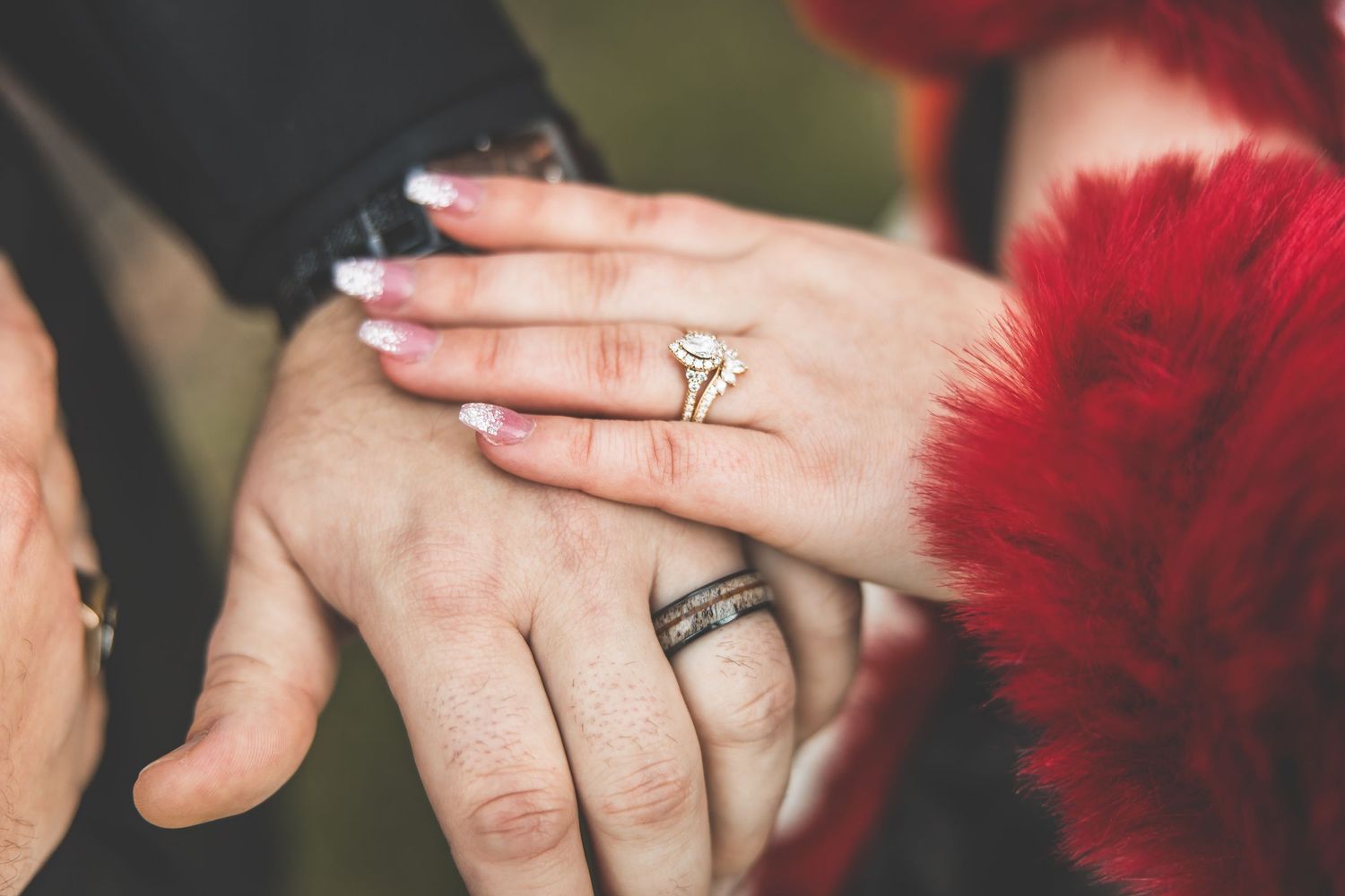 Close-up details of wedding rings and red accessories against a dark background.