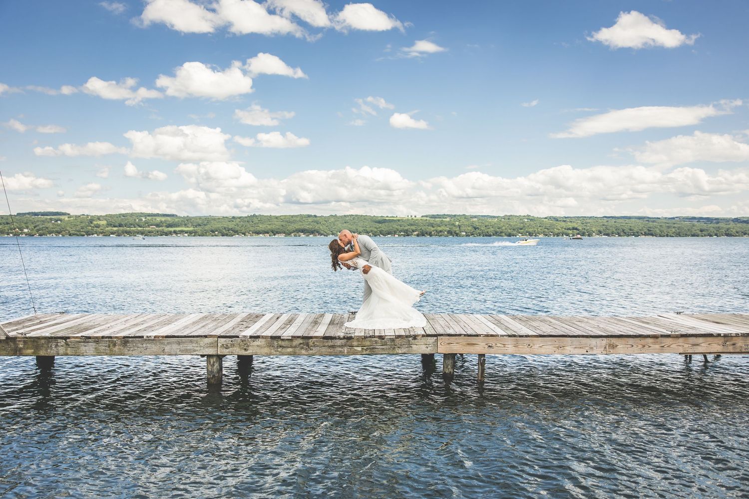 A scenic lakeside dock stretches into blue water under puffy white clouds.