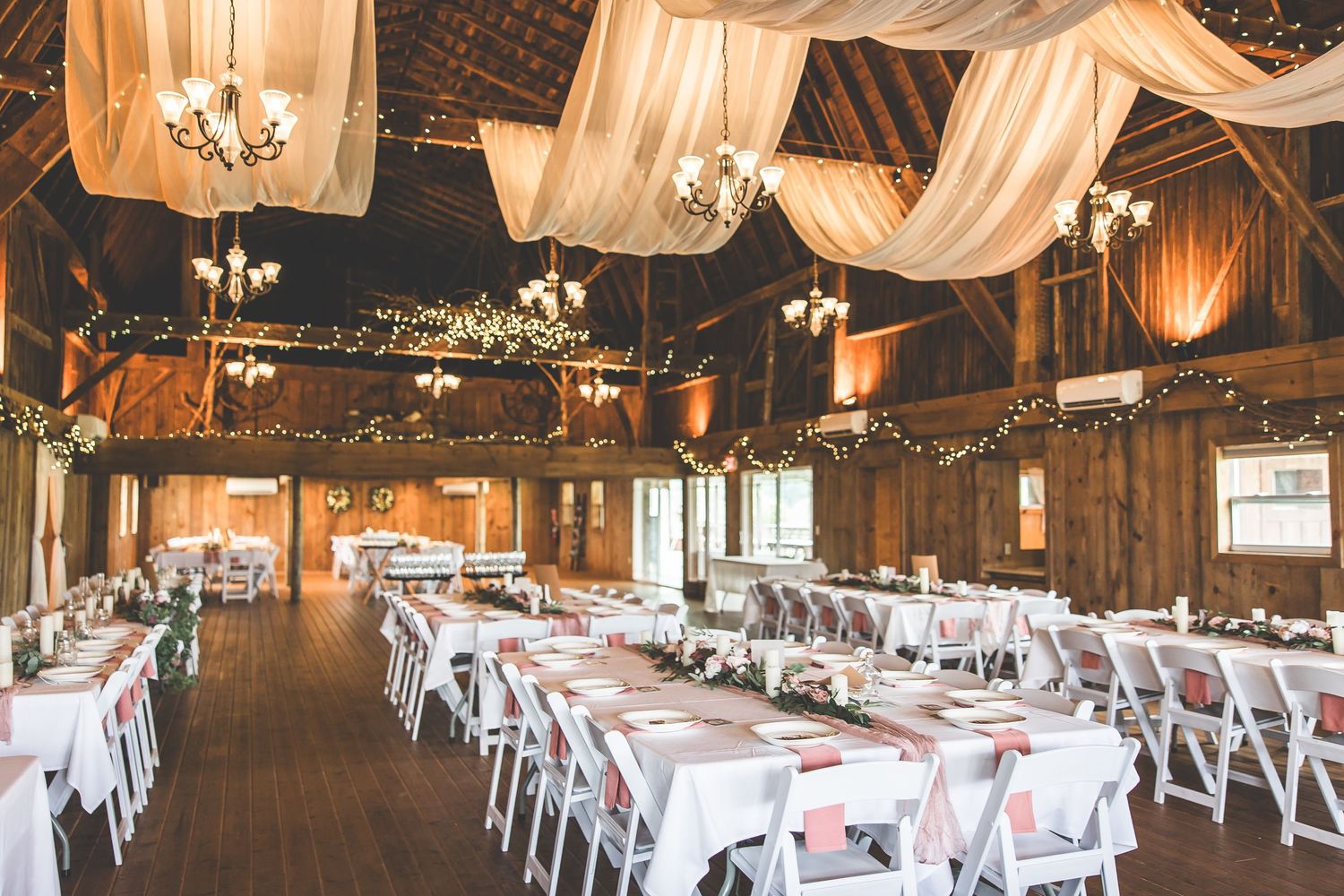 Rustic barn wedding reception venue with elegant white draping and string lights creating a romantic atmosphere.