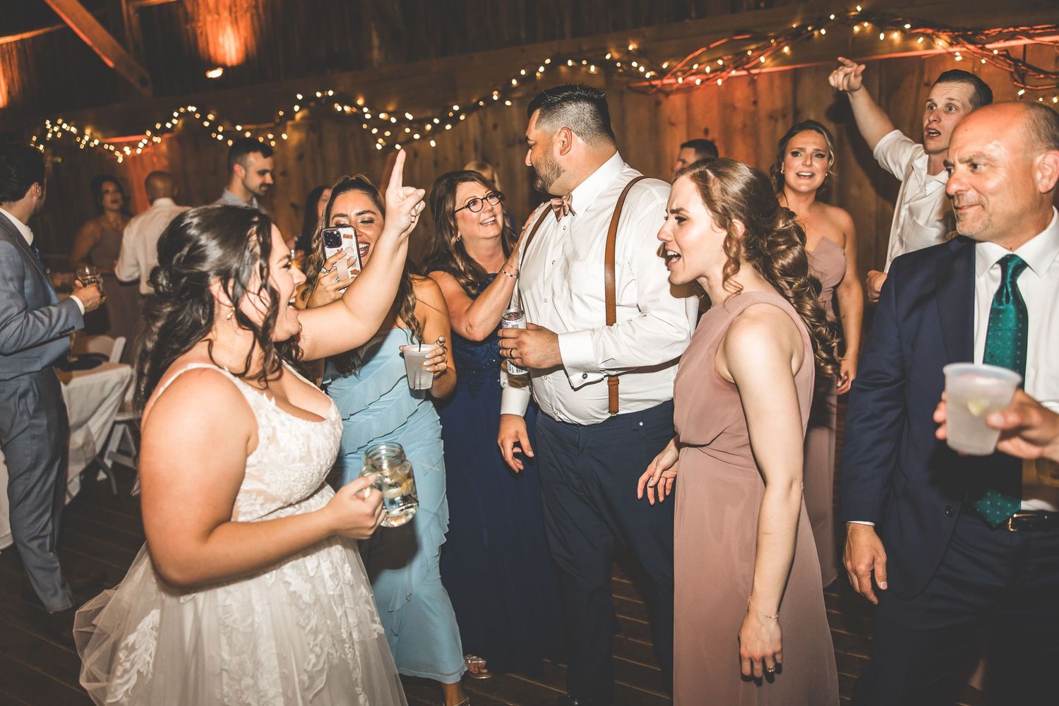 Guests enjoying themselves on a dimly lit dance floor with string lights overhead at a wedding celebration.