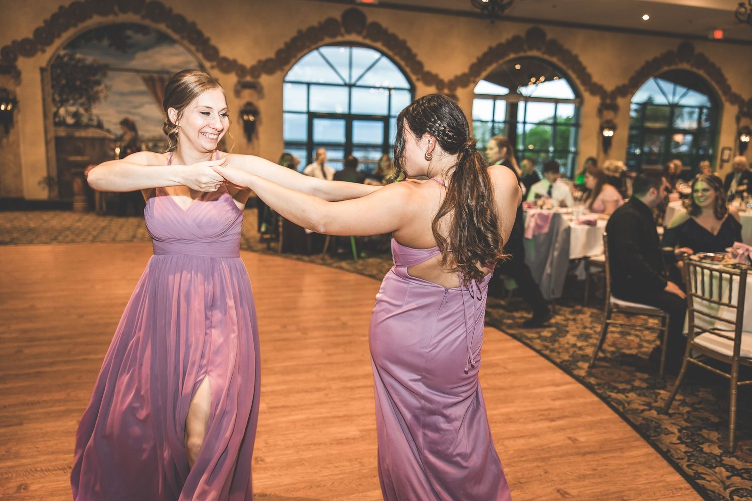 Wedding party members in purple dresses dancing on a wooden dance floor at reception.