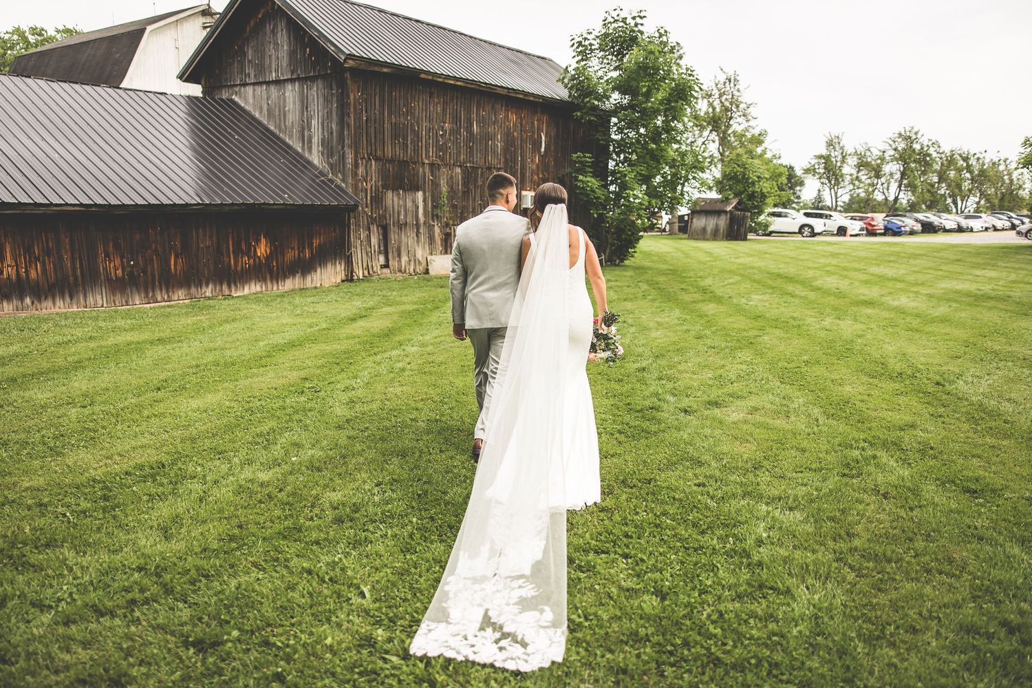 Rustic barn wedding venue with green lawn and wooden buildings in background.
