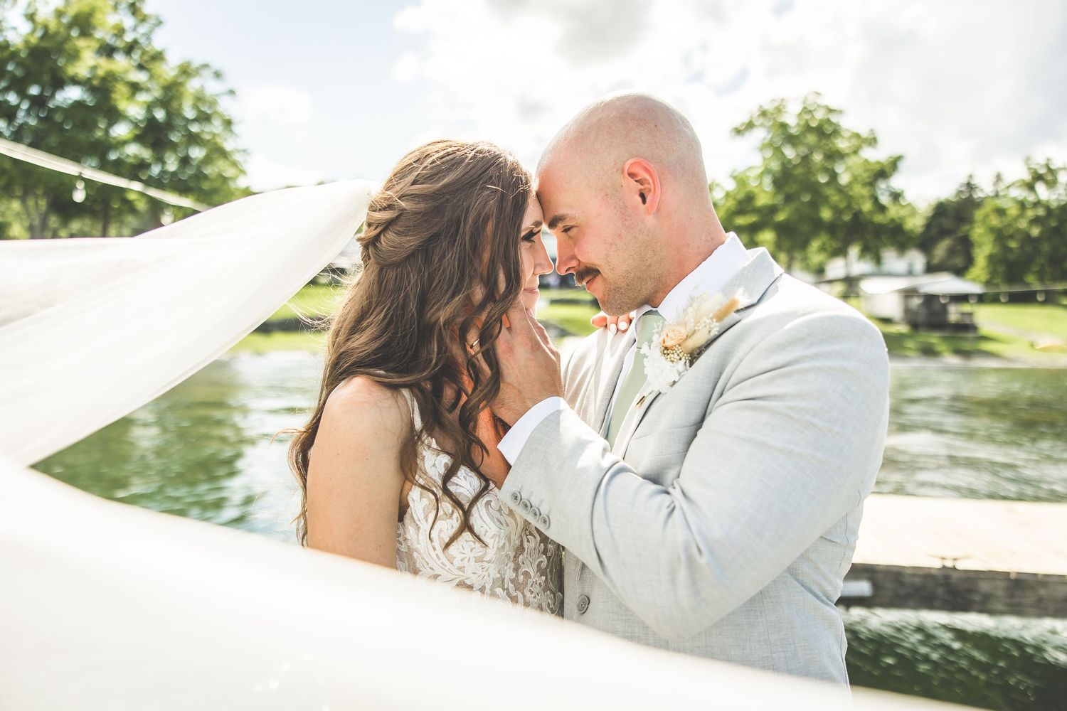 Romantic lakeside wedding portraits with flowing veil and light gray suit.