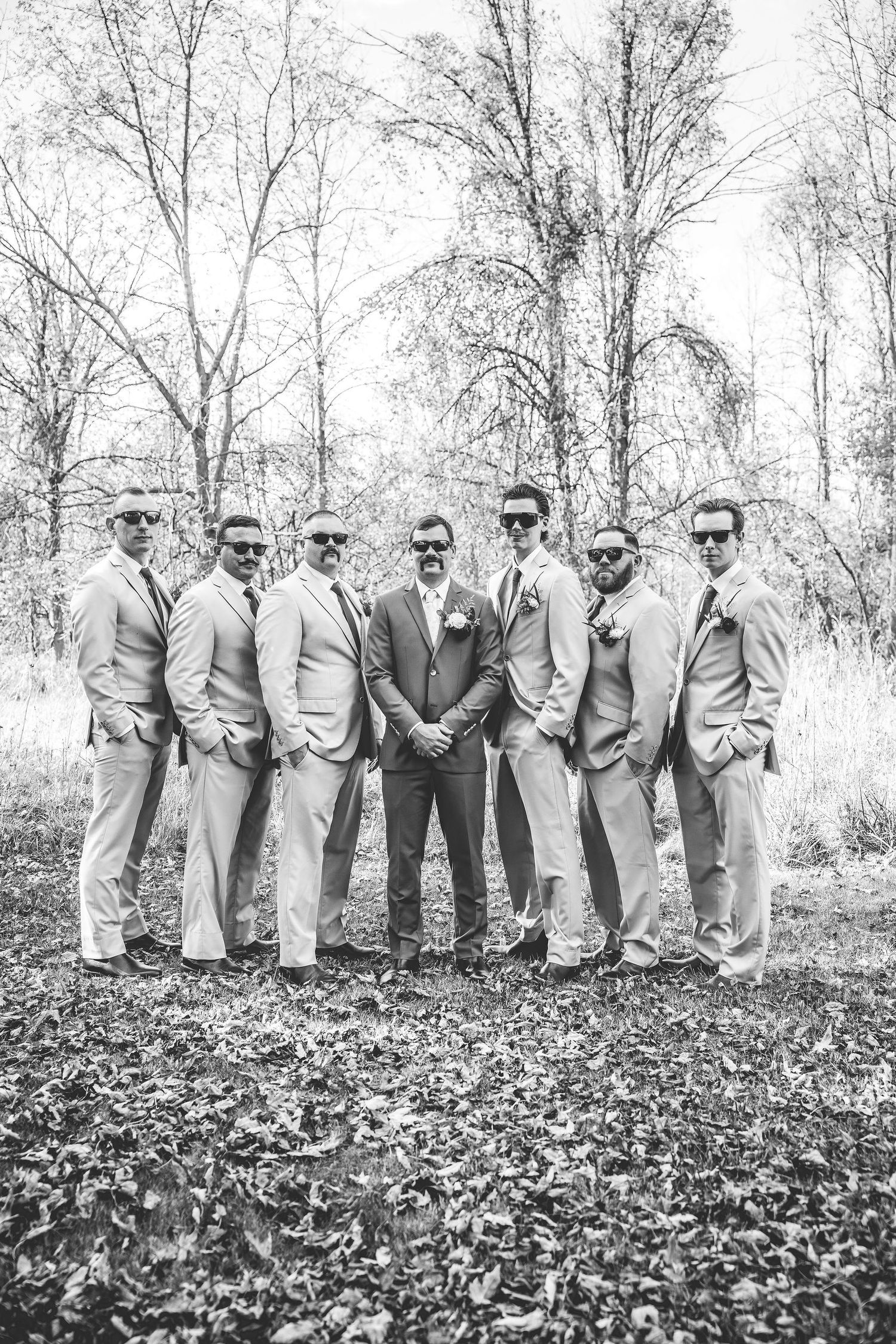 Black and white photo of groomsmen lined up in suits against a backdrop of bare trees.