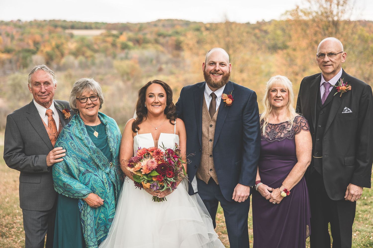 Family formal portraits outdoors with wedding party against autumn landscape background.