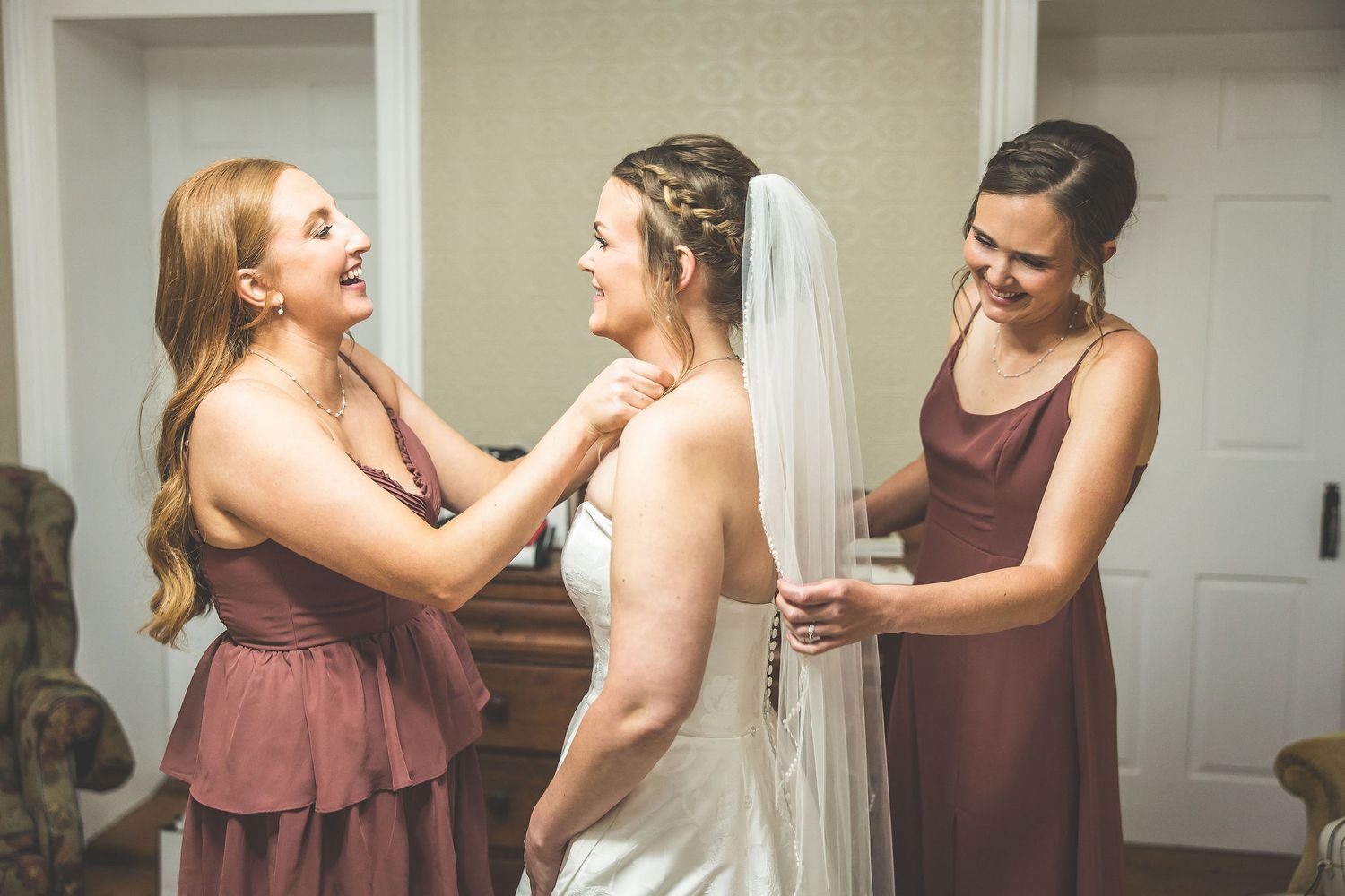 Wedding party members in burgundy dresses share joyful moments while getting ready.