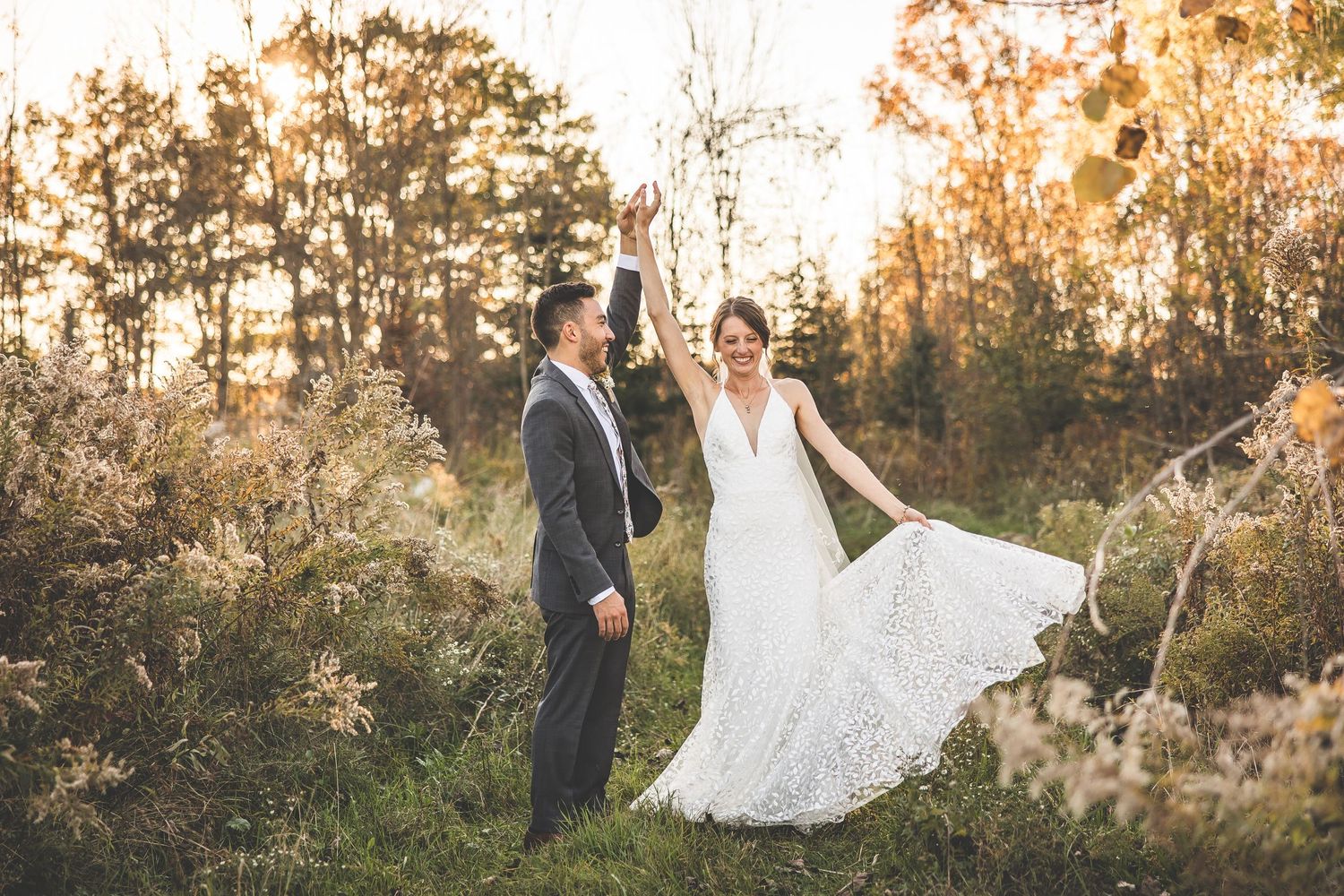 Joyful wedding couple dancing in autumn field with dress flowing in evening light.