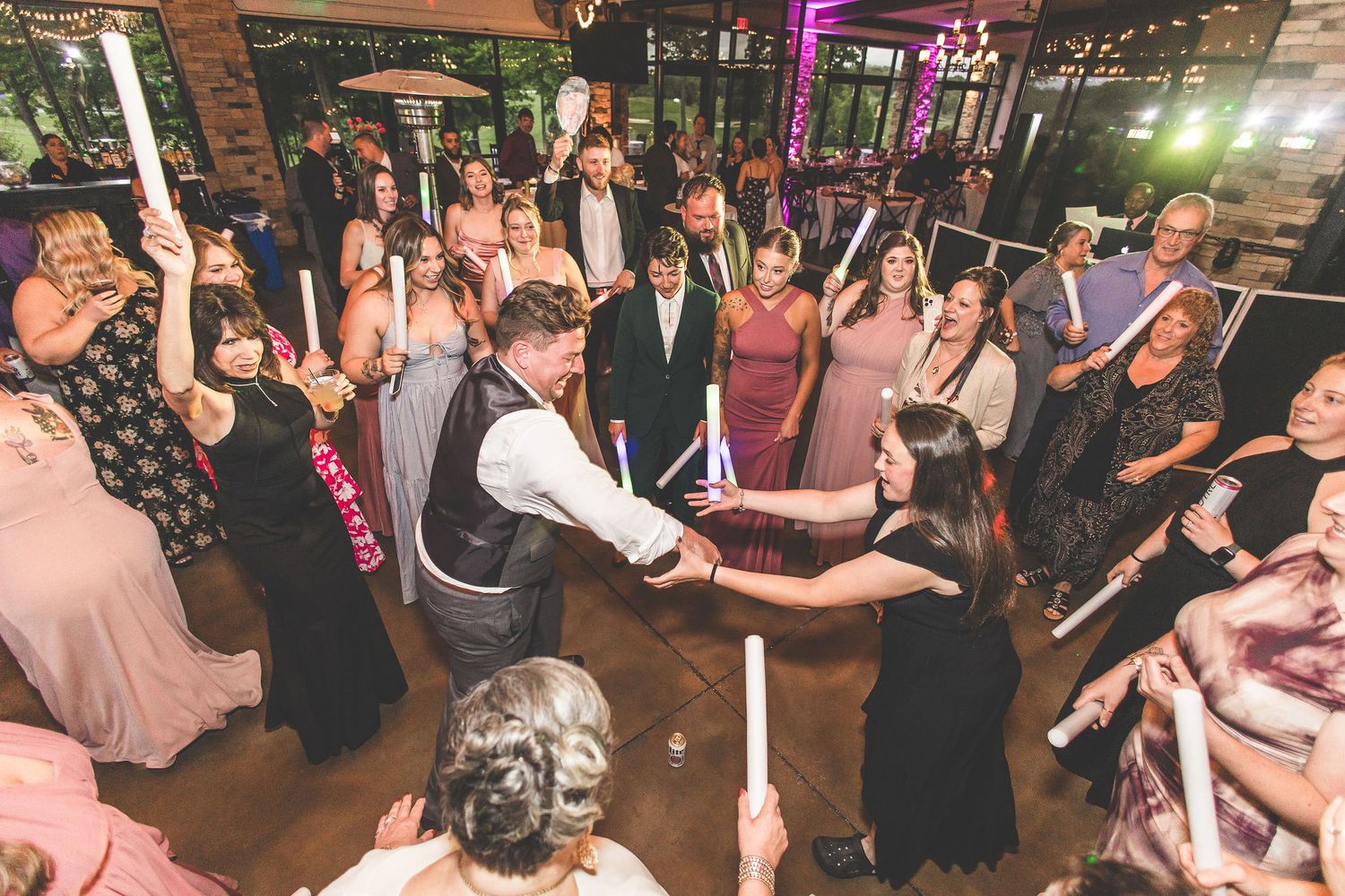 Large group of wedding guests dancing and celebrating on a dimly lit dance floor.