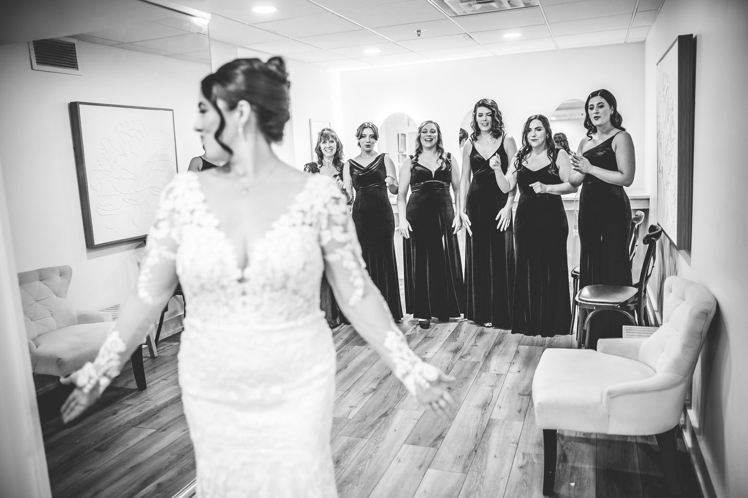 Black and white panoramic view of bridesmaids watching wedding dress preparations.