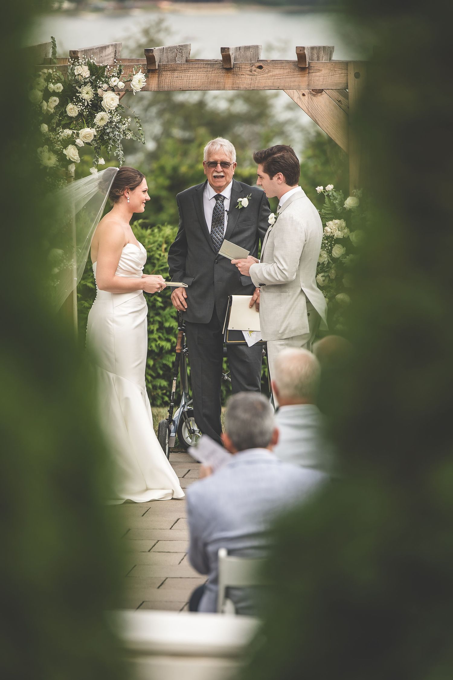 Intimate wedding ceremony moment captured through foliage at wooden arch altar.