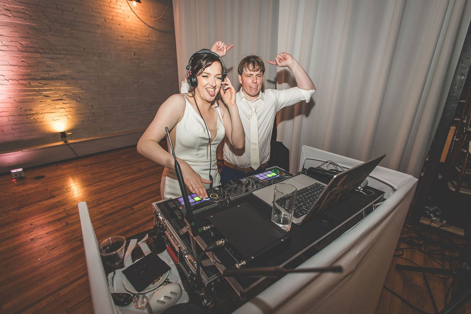 DJs performing at a wedding reception behind professional equipment with ambient lighting.
