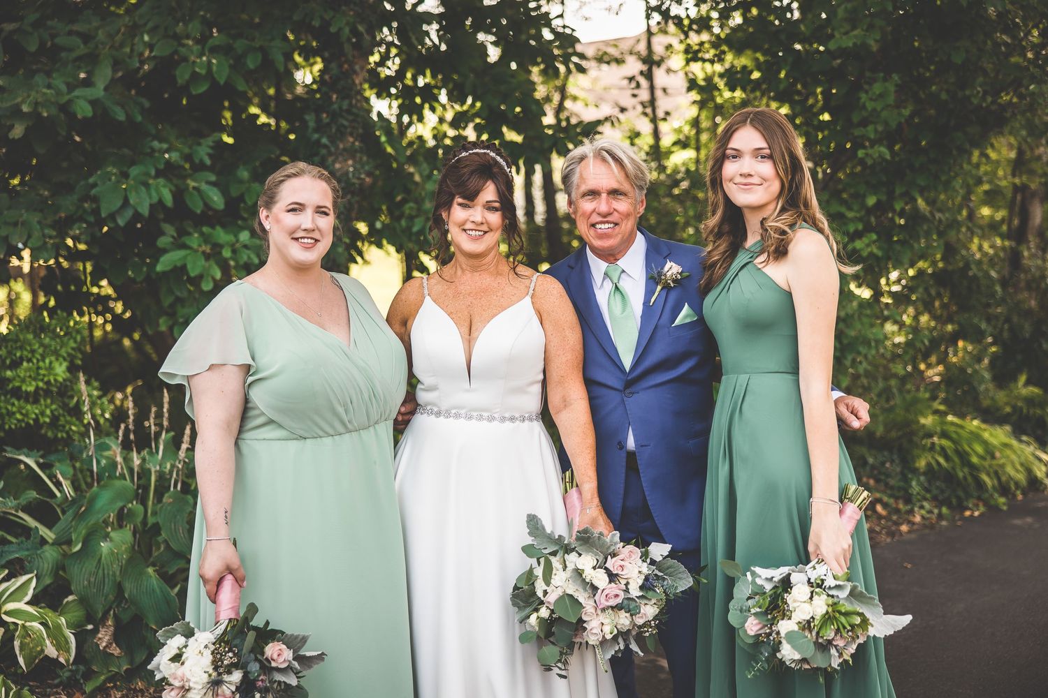 Wedding party in sage green and white attire poses outdoors.