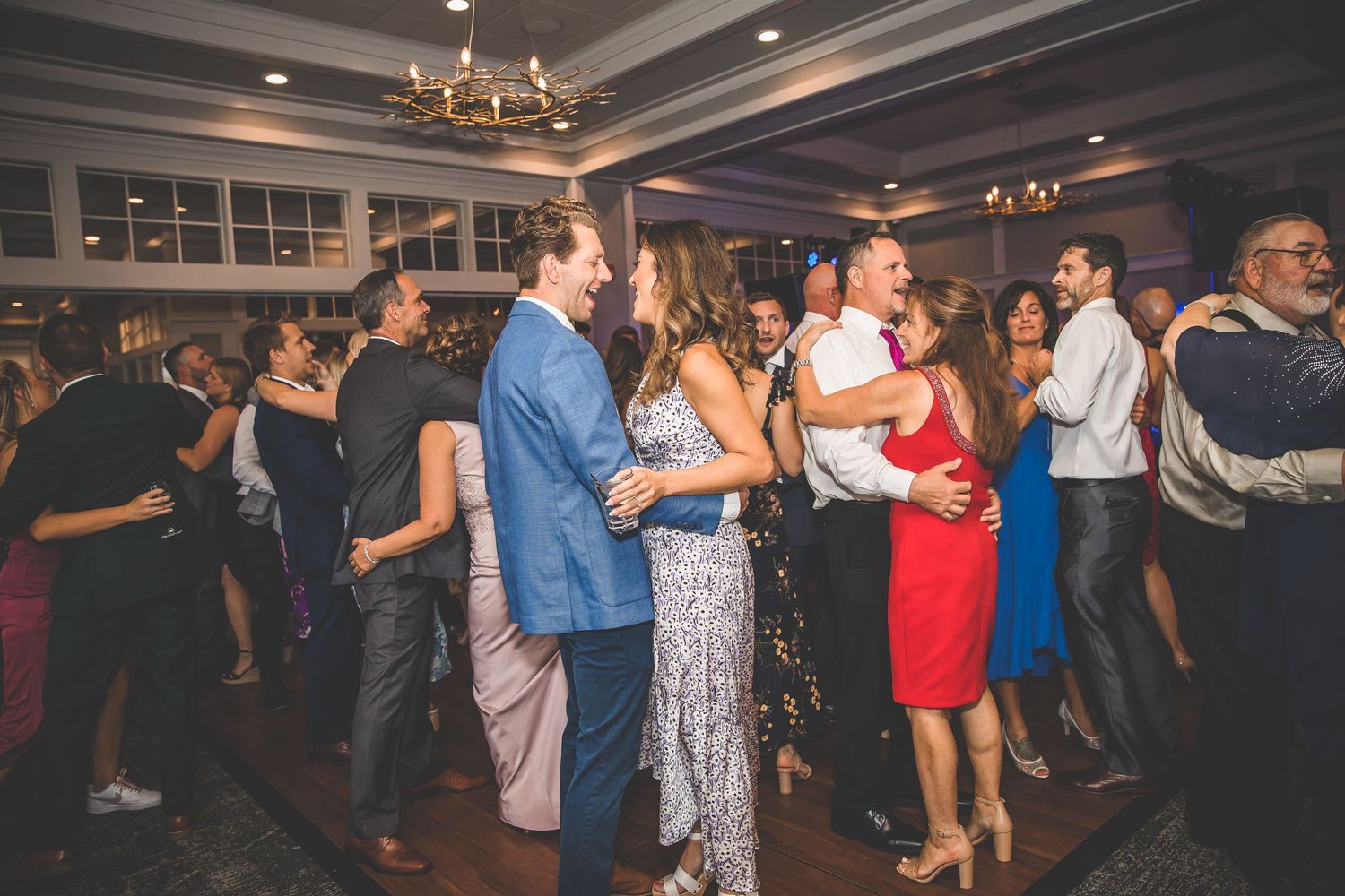 Energetic crowd dancing at a wedding reception in a ballroom with elegant lighting and decor.