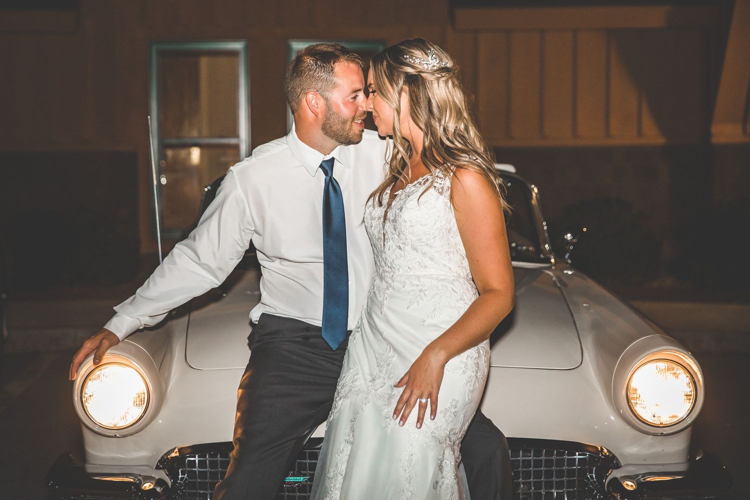 Romantic nighttime portraits with couple and classic car at wedding venue.