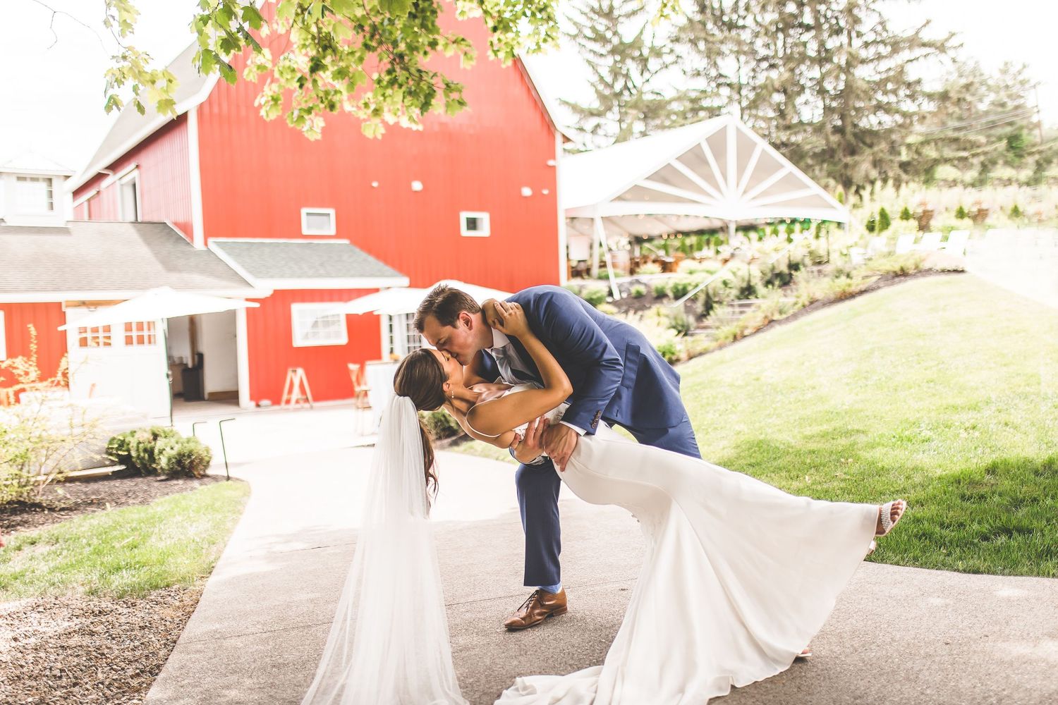Wedding couple shares intimate moments along a garden path near a red barn.