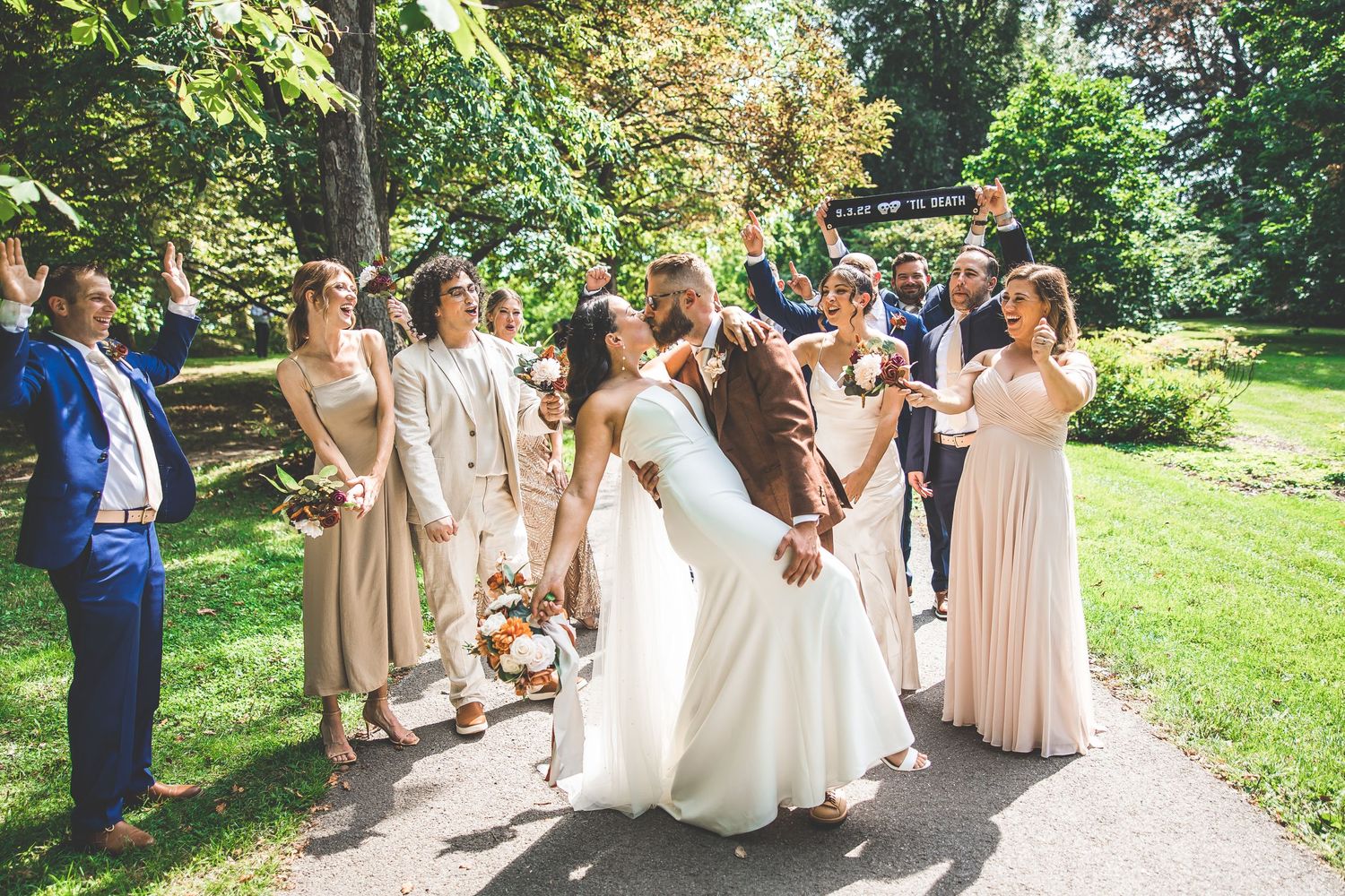 Wedding party poses on garden path with bridesmaids in neutral dresses.