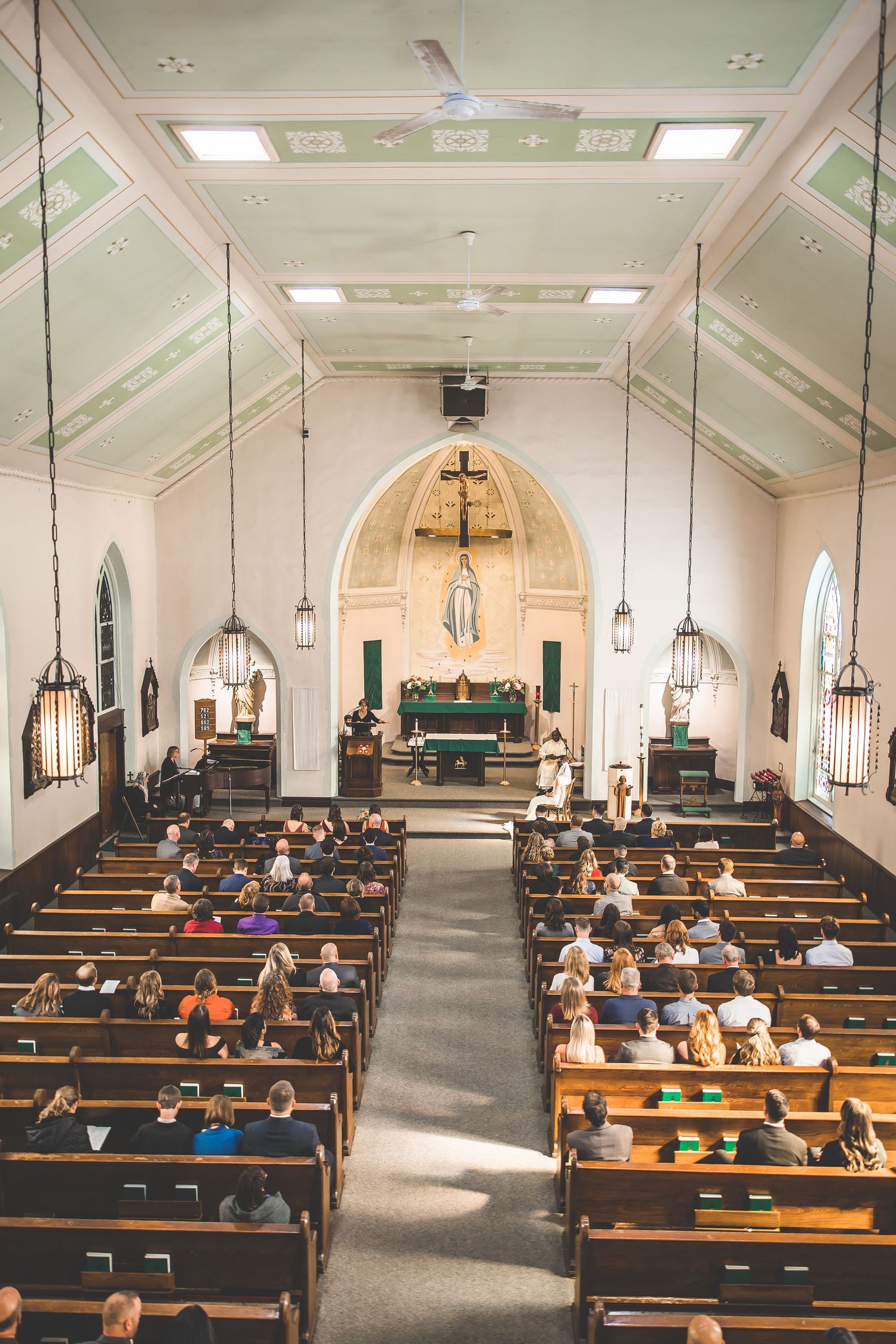 Interior view of a church sanctuary with wooden pews and hanging pendant lights.