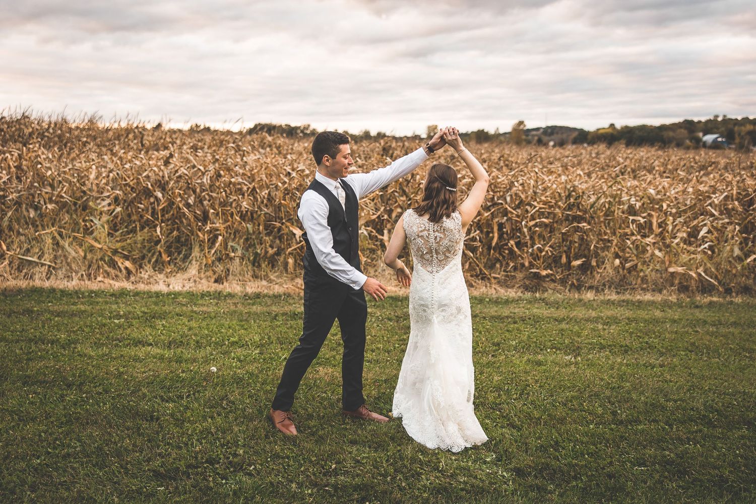 Newlyweds dancing playfully in front of a cornfield on their wedding day.