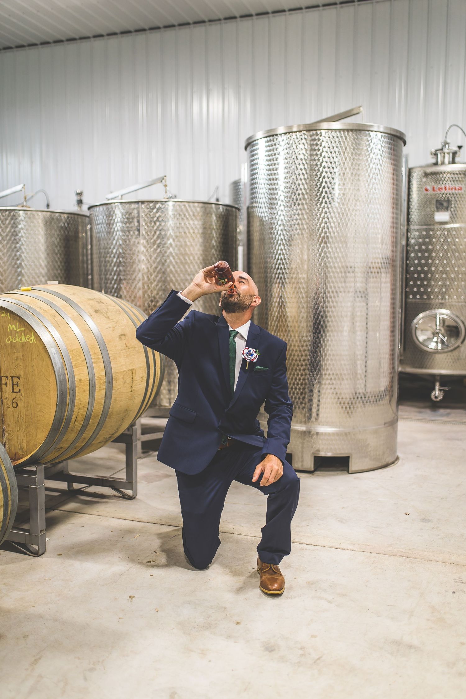 Groomsmen pose playfully among large metal wine tanks in cellar setting.