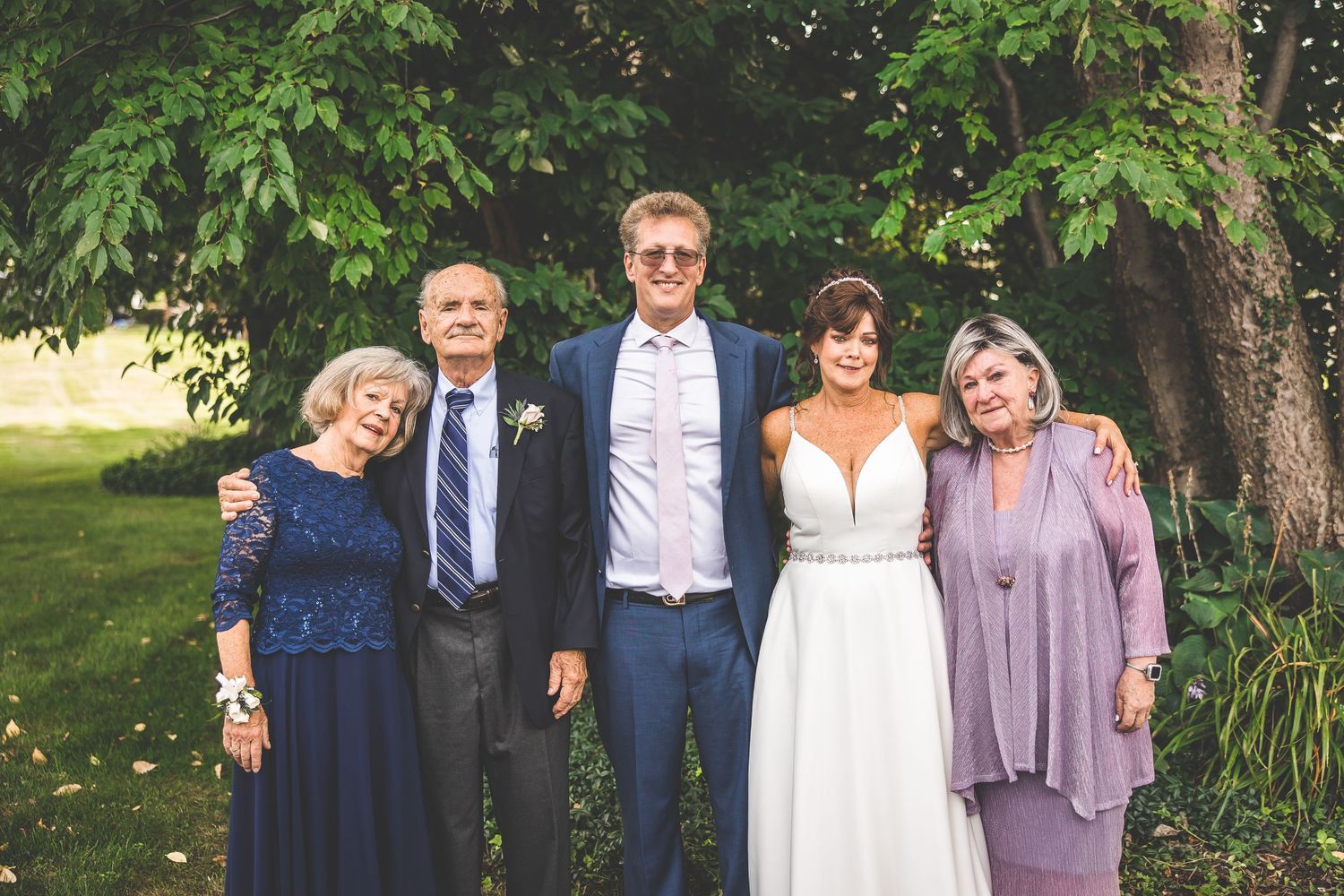 Wedding guests in formal attire posing for group photos in garden setting.