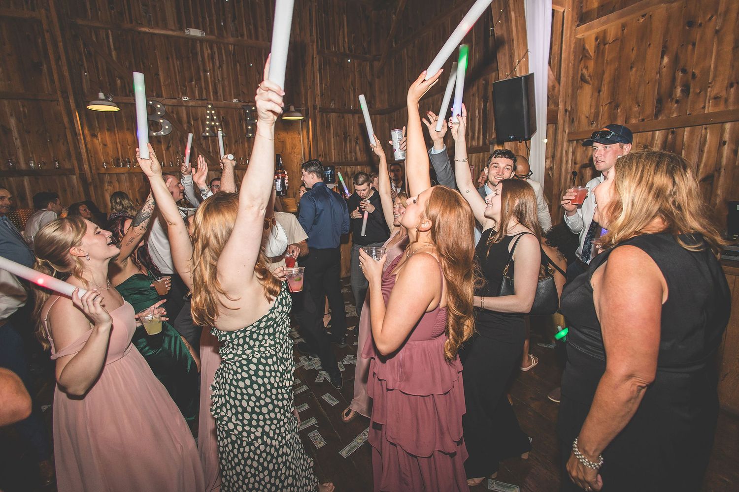Lively crowd dancing and celebrating at a wedding reception in a rustic barn venue.