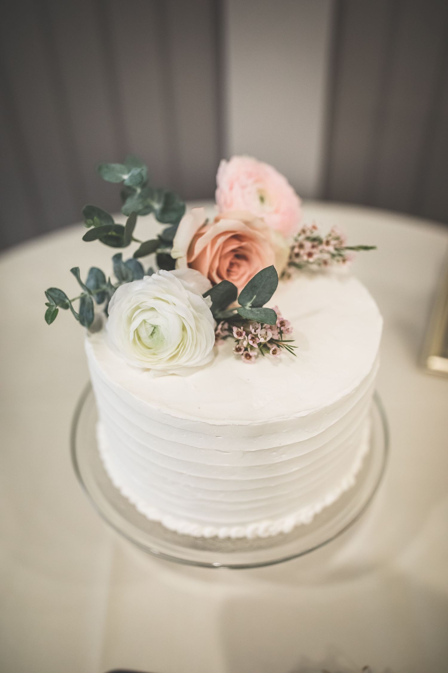 White wedding cake decorated with fresh pink roses and eucalyptus leaves.