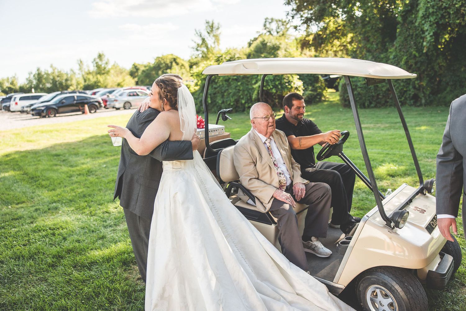 Wedding party riding in golf carts across a sunny green lawn.
