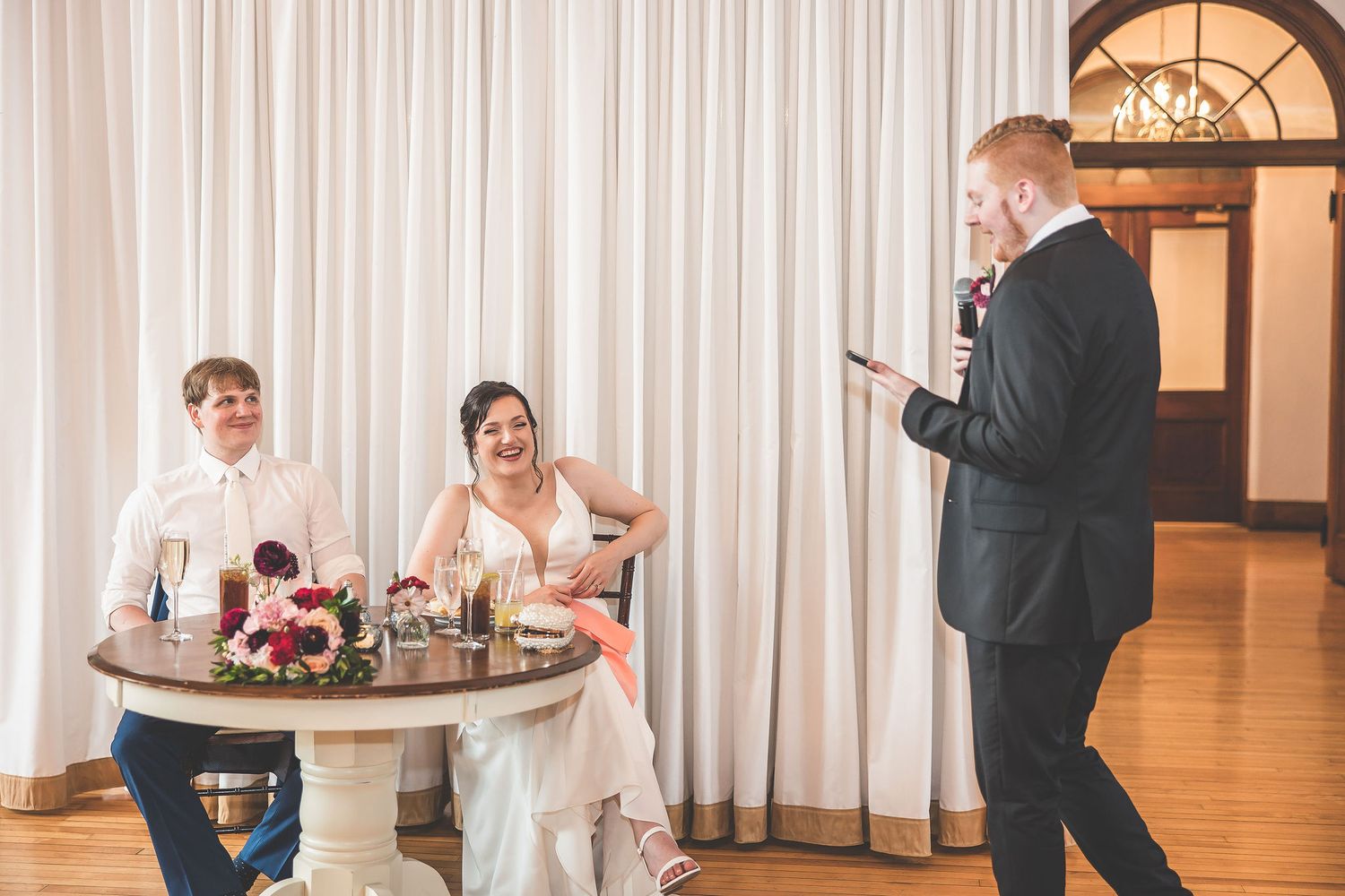 A candid moment during wedding toasts at an elegant indoor reception venue.