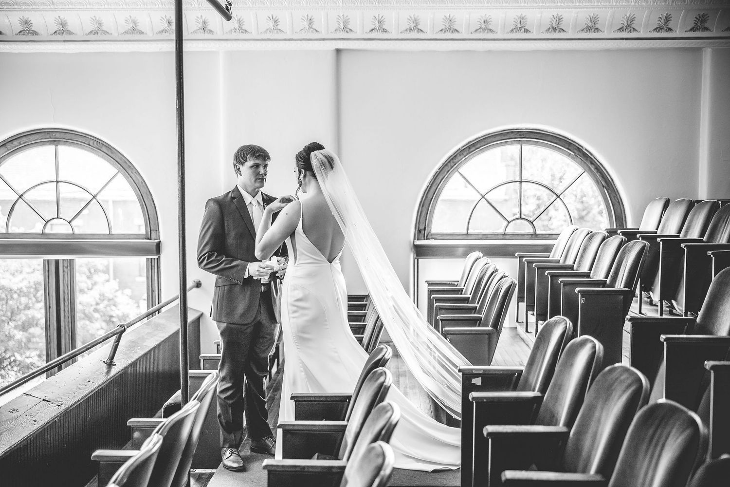 Romantic wedding scene in a historic theater with arched windows and red velvet seating.
