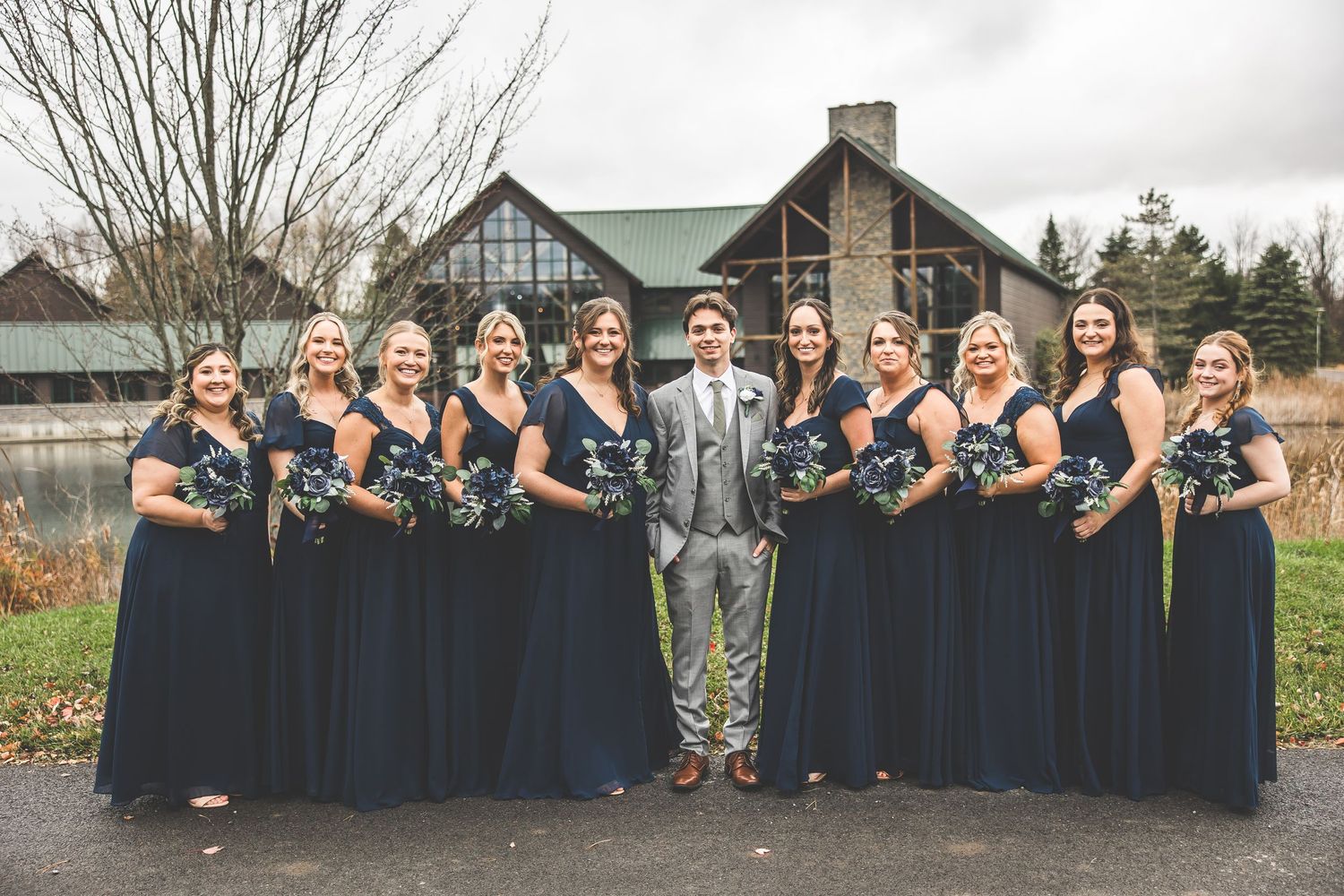Large wedding party in navy and gray attire poses for group photos outside.
