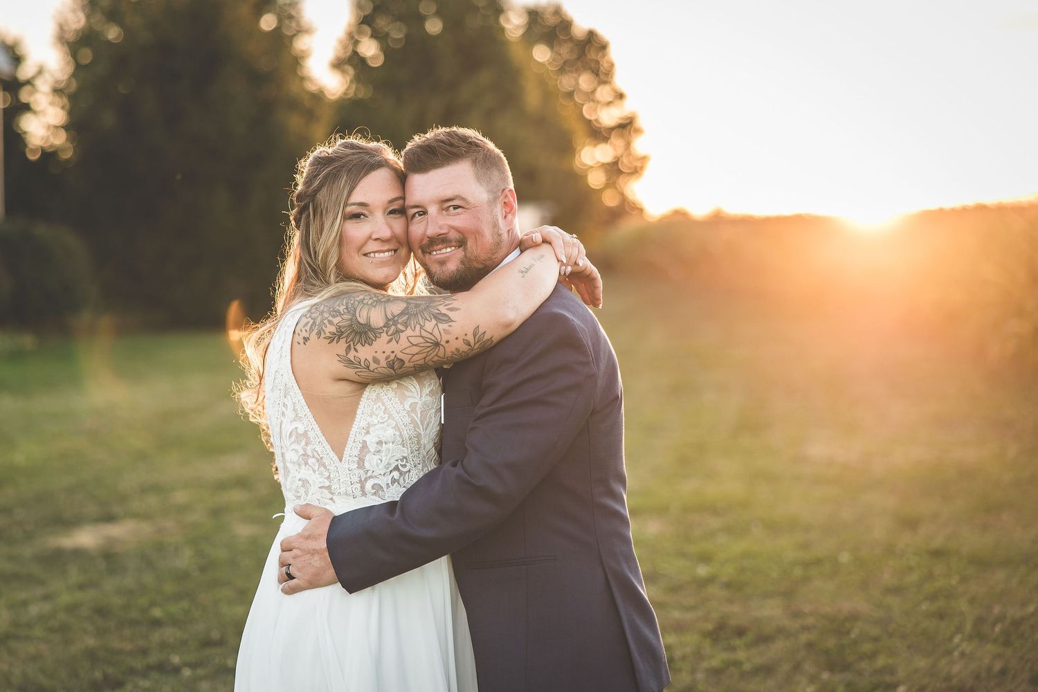 Intimate sunset wedding portrait with couple embracing in front of trees.