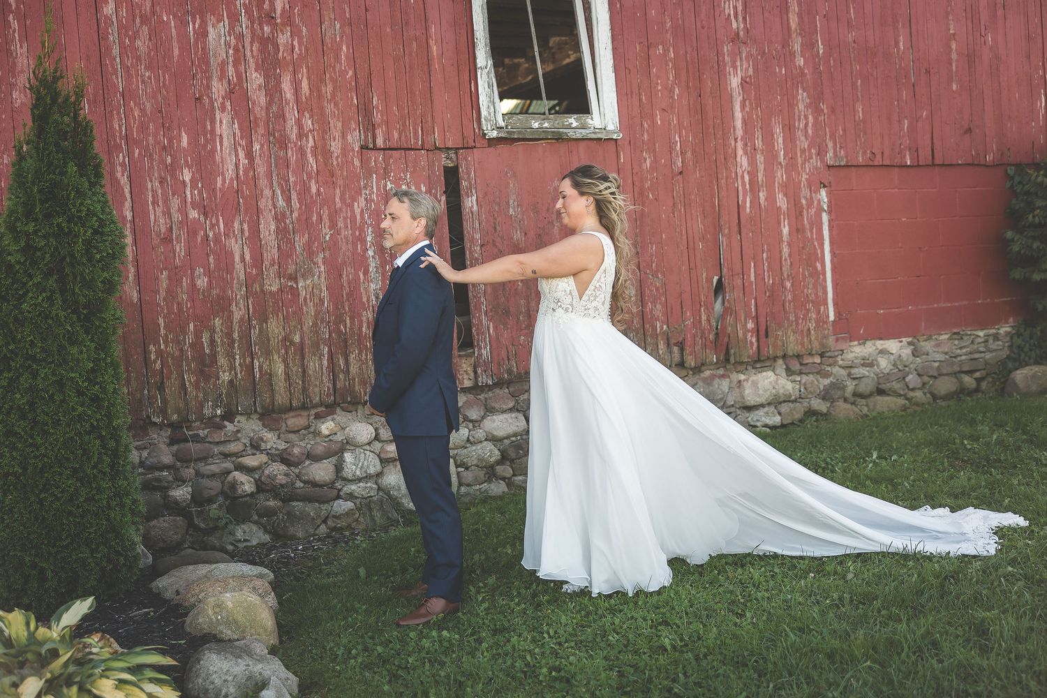 Wedding couple poses against weathered red barn exterior for romantic photos.