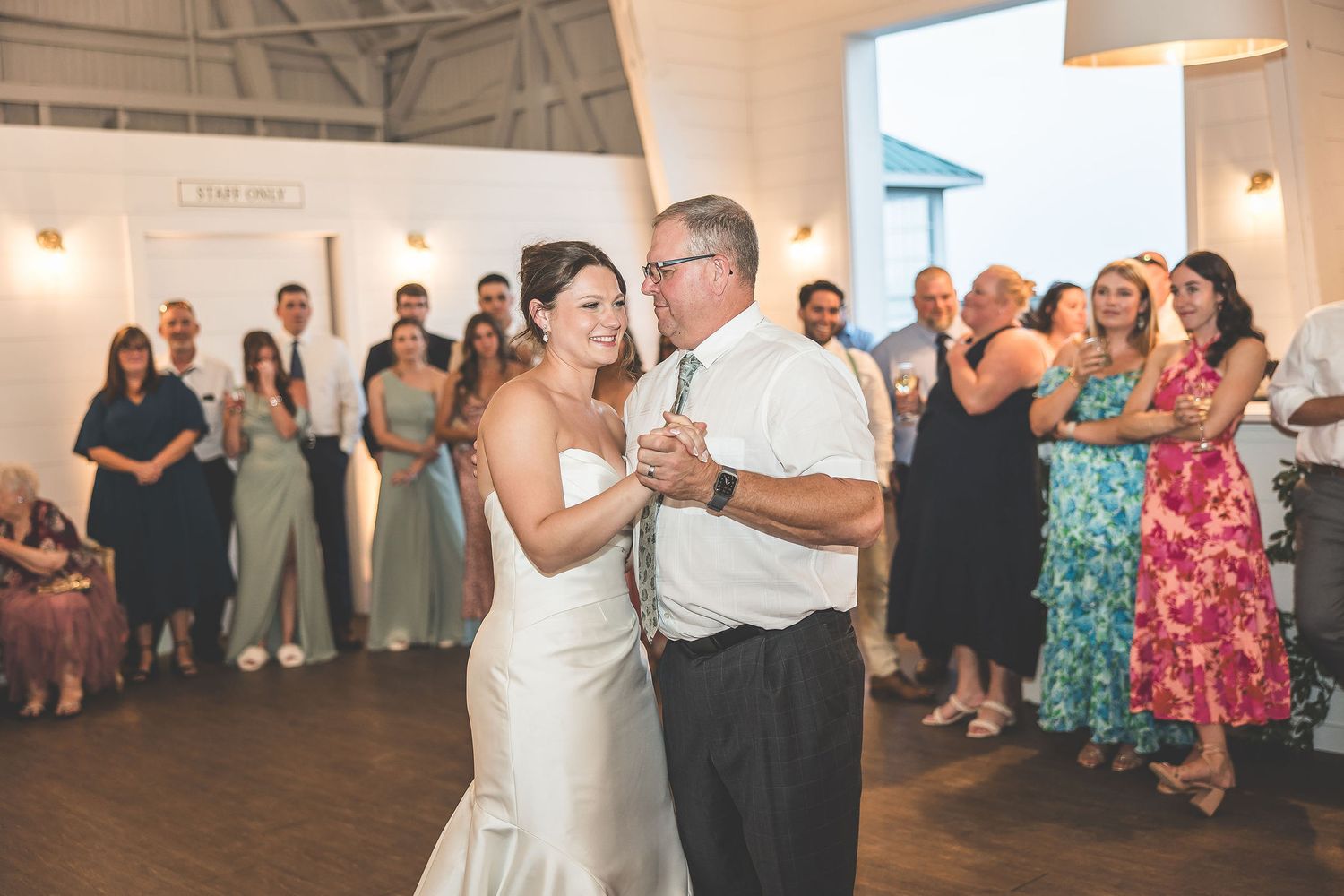 Wedding reception guests dance and celebrate in a rustic venue with string lights overhead.