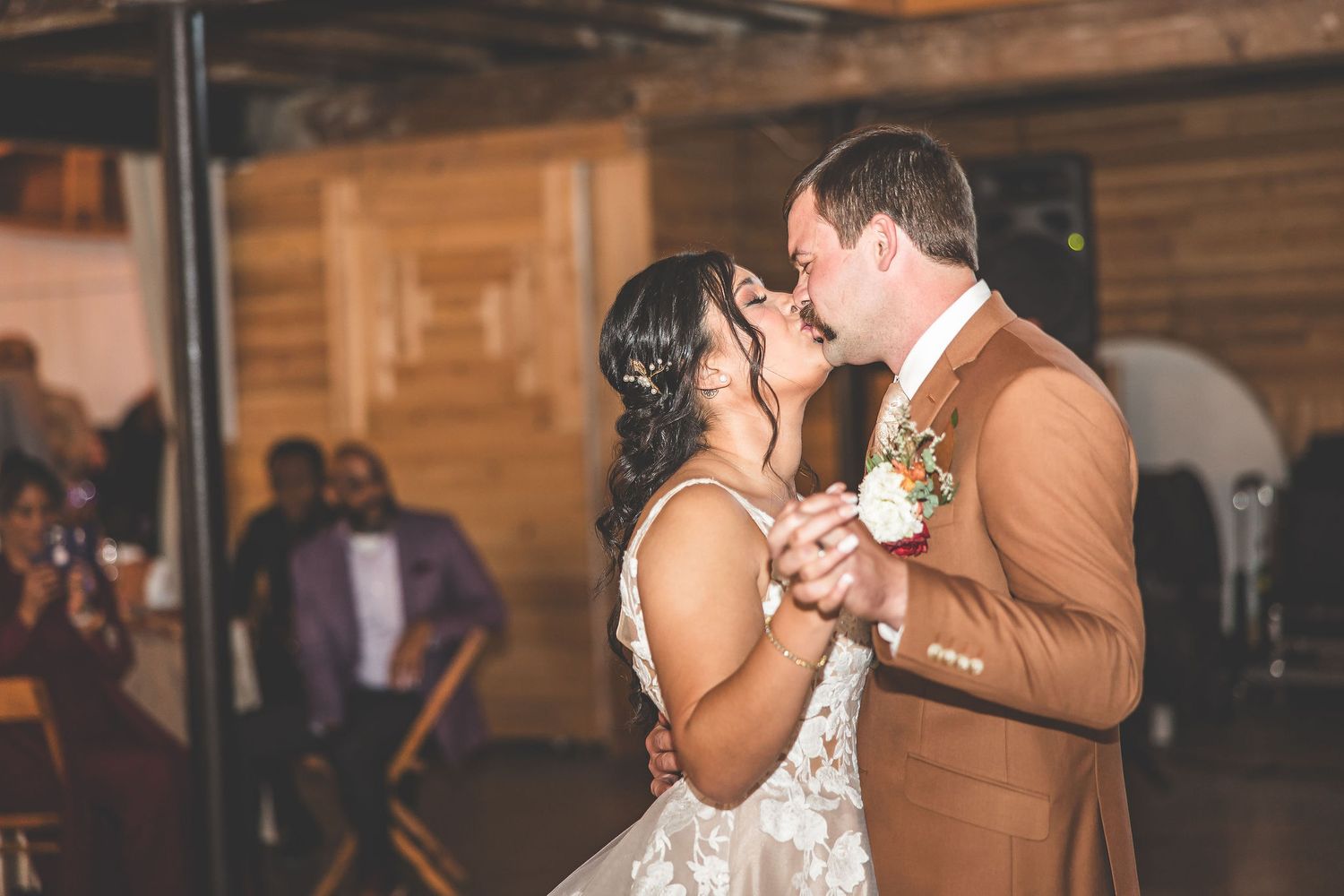 A romantic slow dance moment captured at a rustic barn wedding reception with string lights overhead.