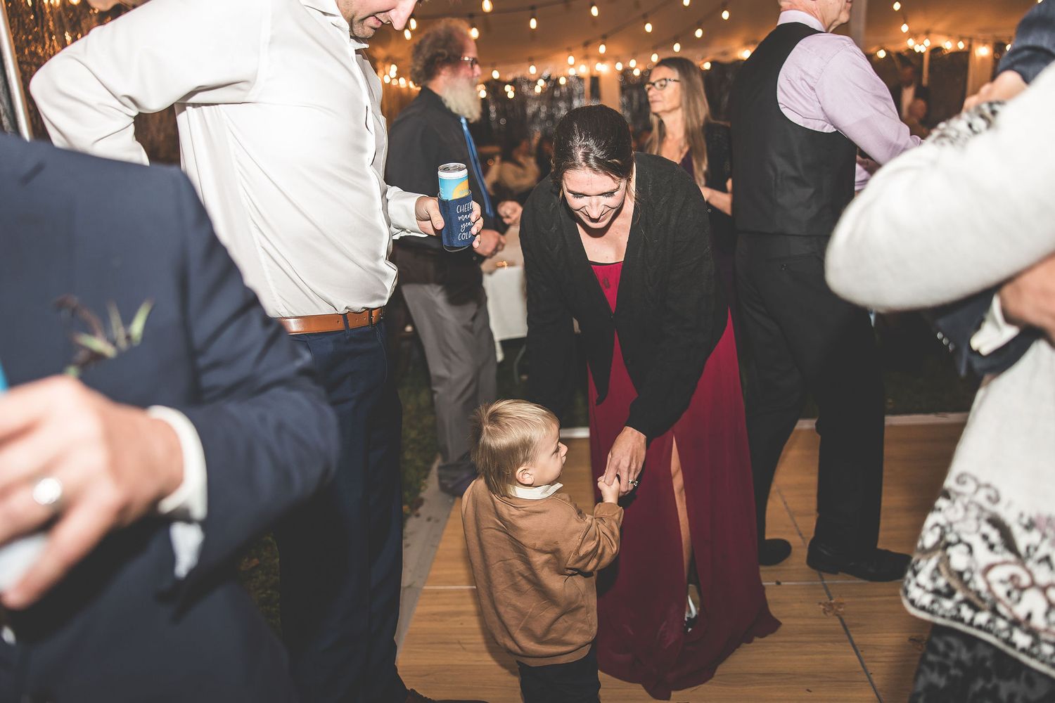Guests dancing and celebrating at a dimly lit wedding reception with string lights overhead.