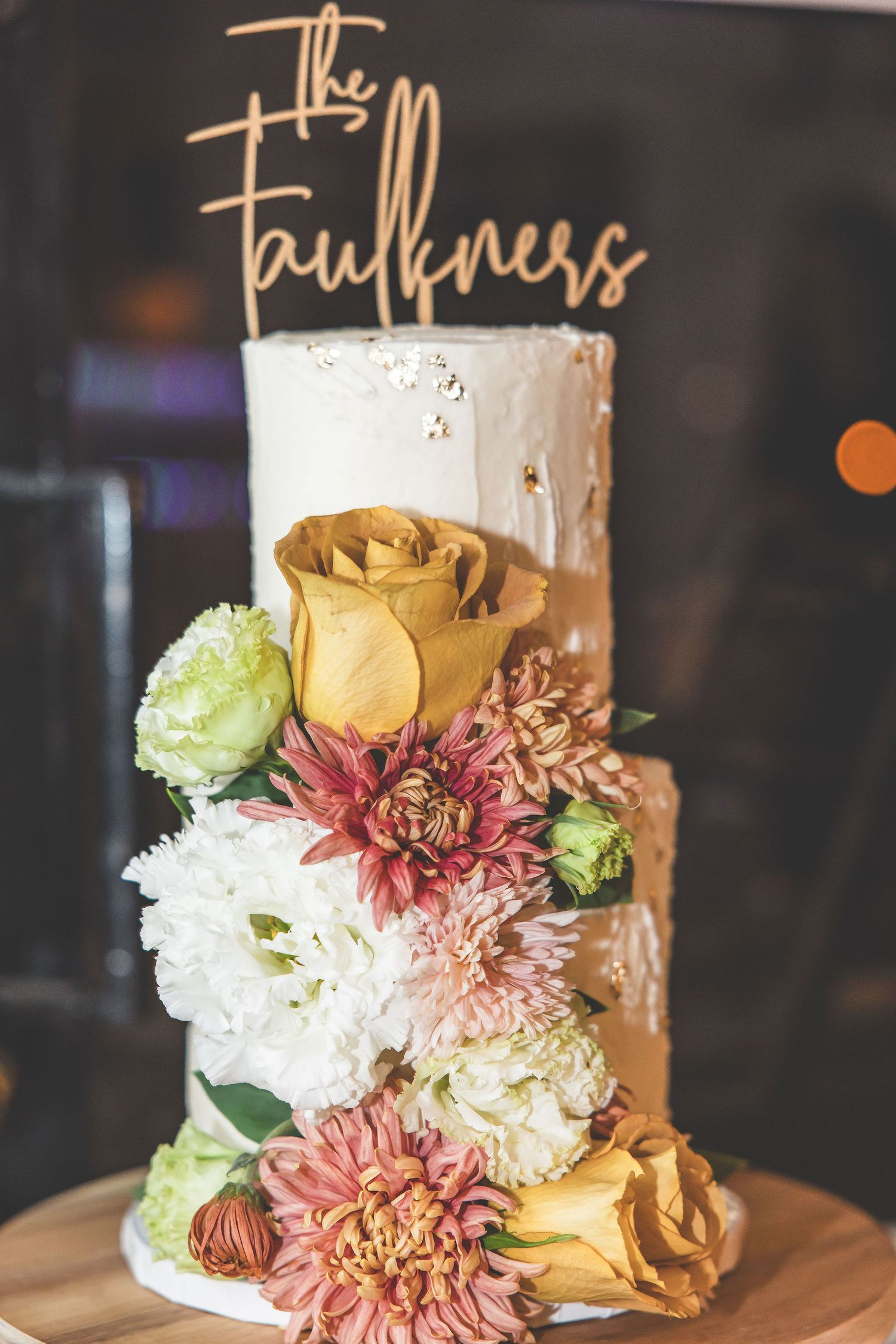 Elegant white wedding cake decorated with fresh pink, yellow and white flowers.