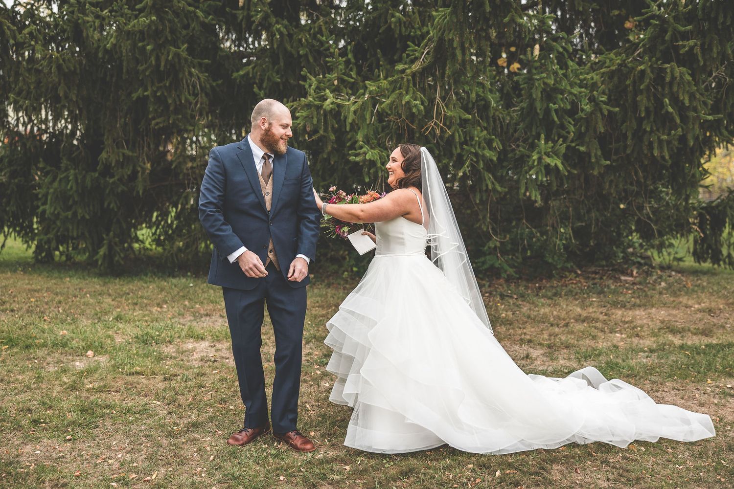 A romantic first look moment between a couple in wedding attire against a backdrop of evergreen trees.